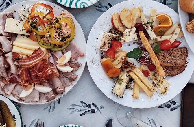 Dva tal&iacute;ře s uzeninami, s&yacute;rem, zeleninou a ovocem na stole.