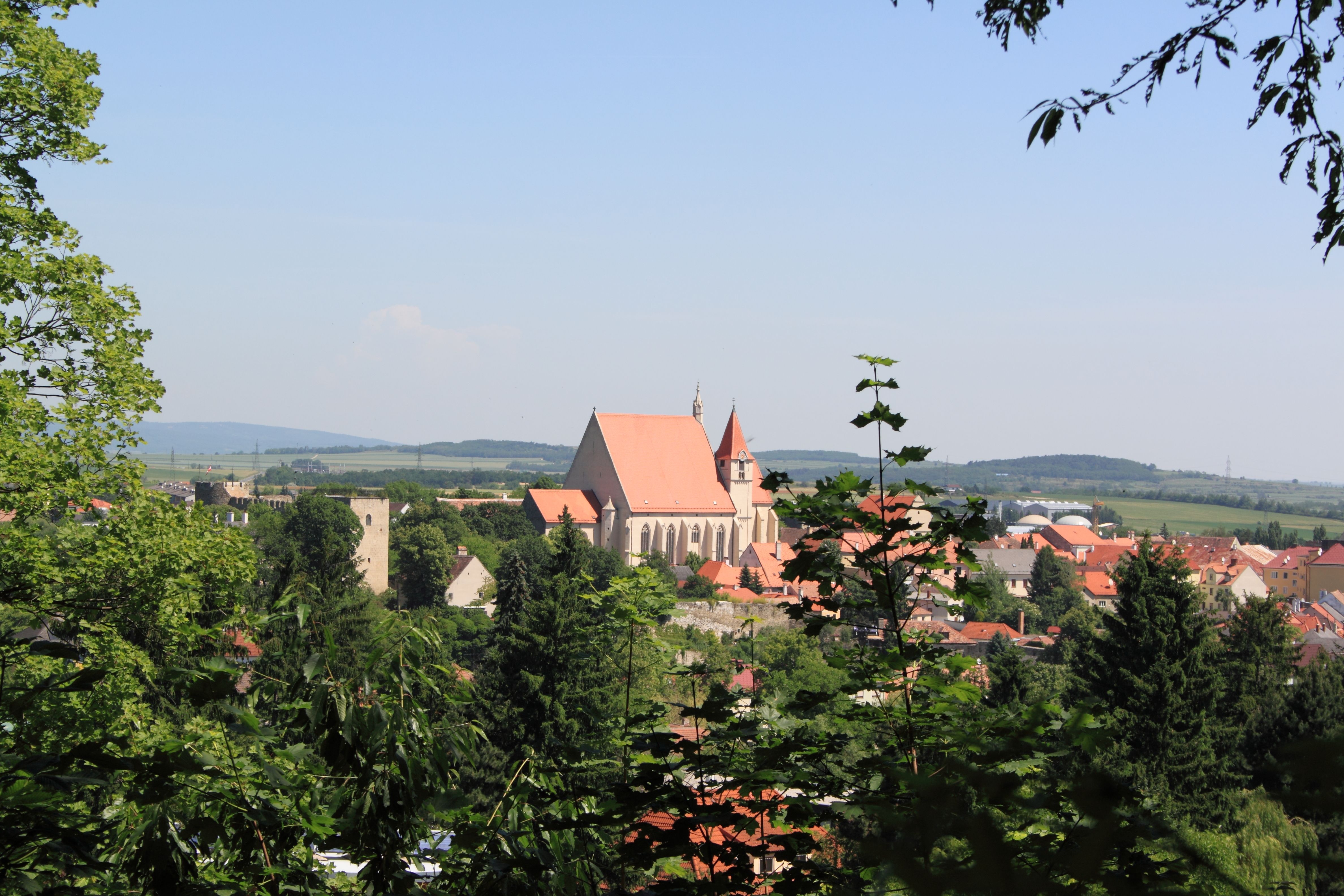 Panoramatický pohled na Eggenburg s kostelem a okolními budovami, obklopený stromy a kopci v pozadí.