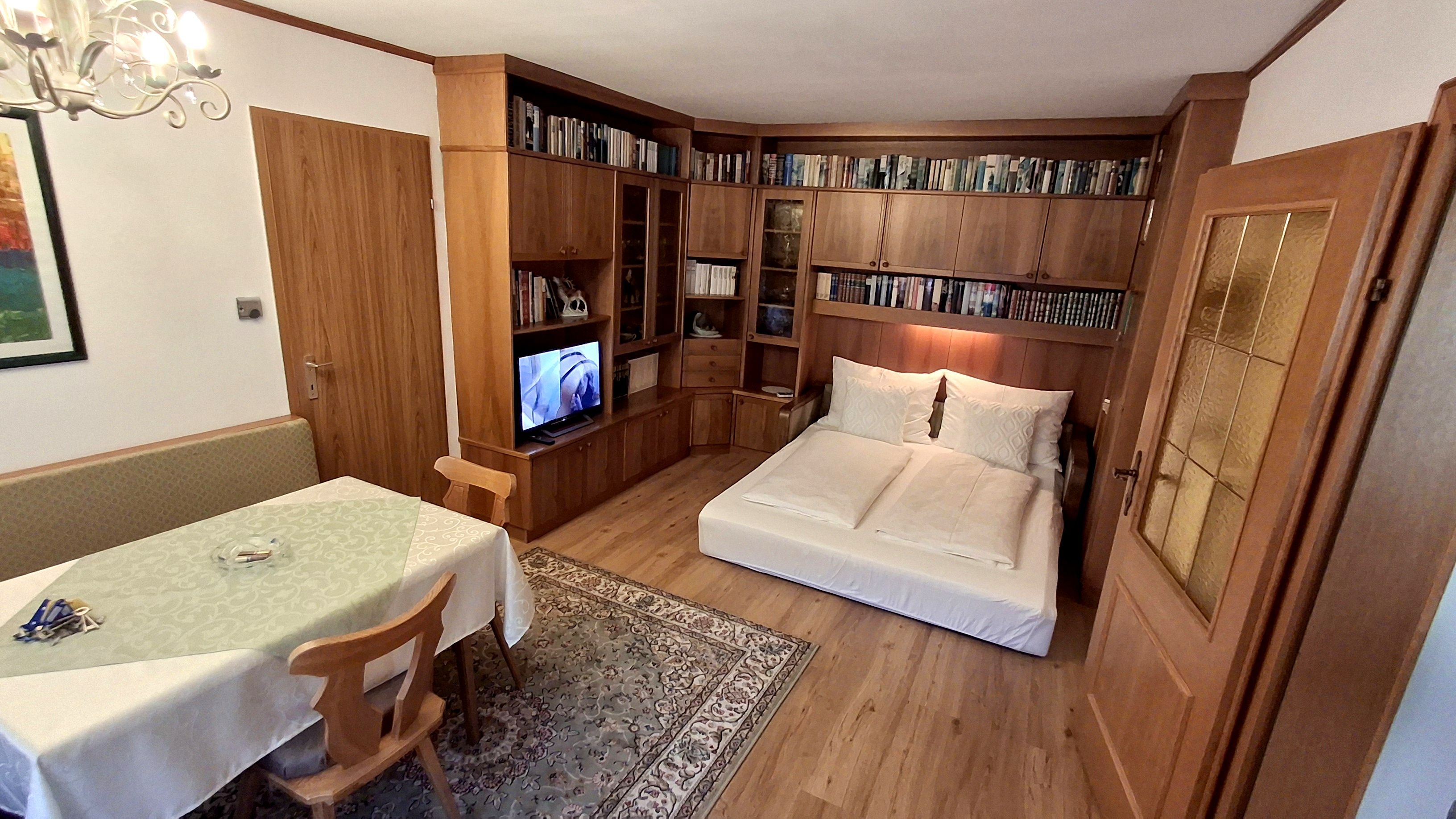 Obývací pokoj s rozkládací pohovkou, knihovnou, jídelním stolem a TV.