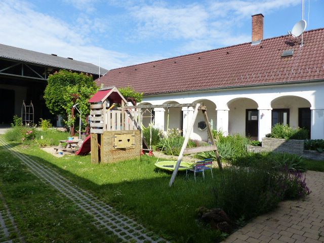 Vnitřní dvůr s dětským hřištěm, obklopený budovou s červenými střešními taškami a bílými zdmi.