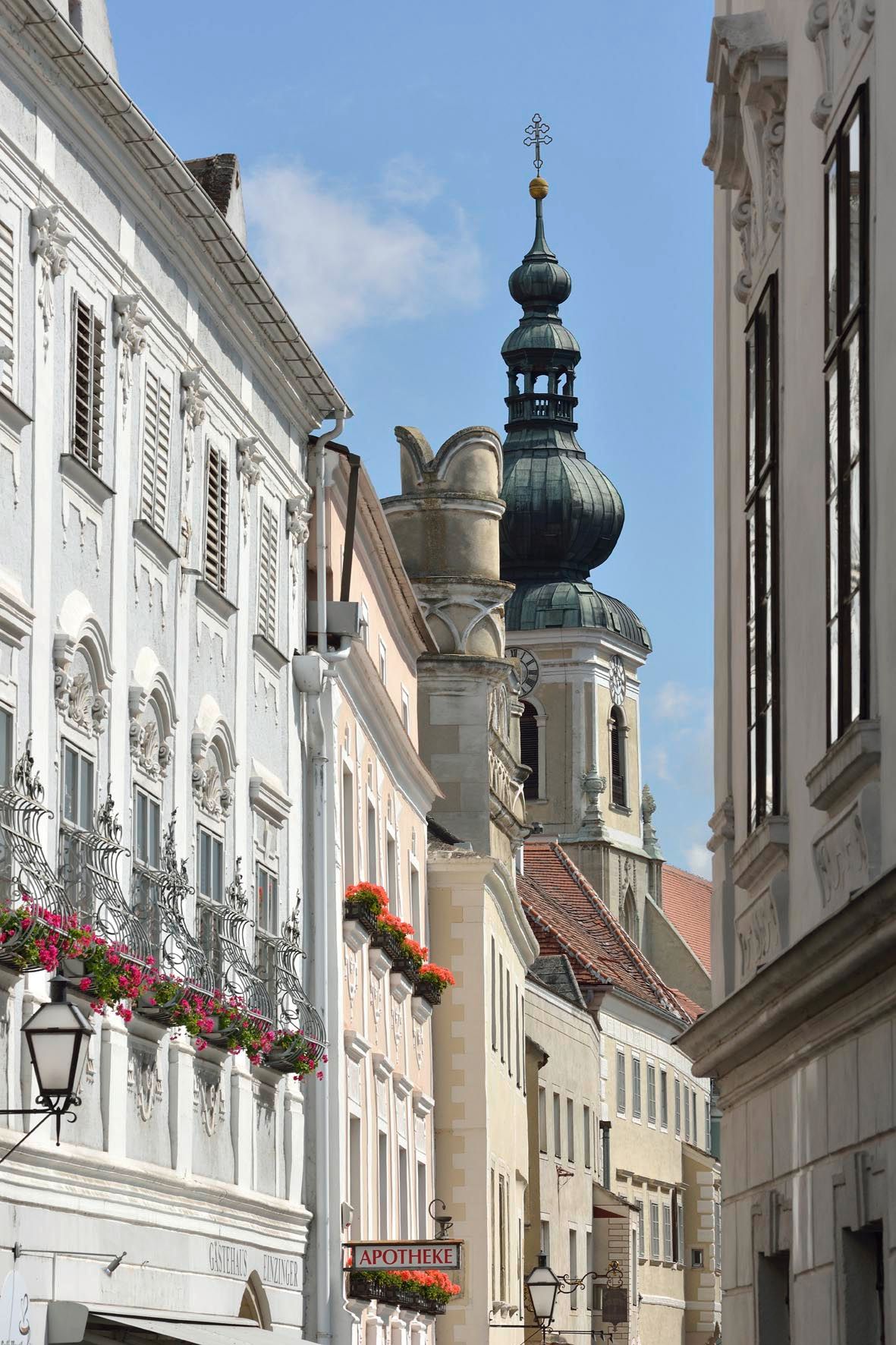 Uliční scéna s historickými budovami a kostelní věží v pozadí.