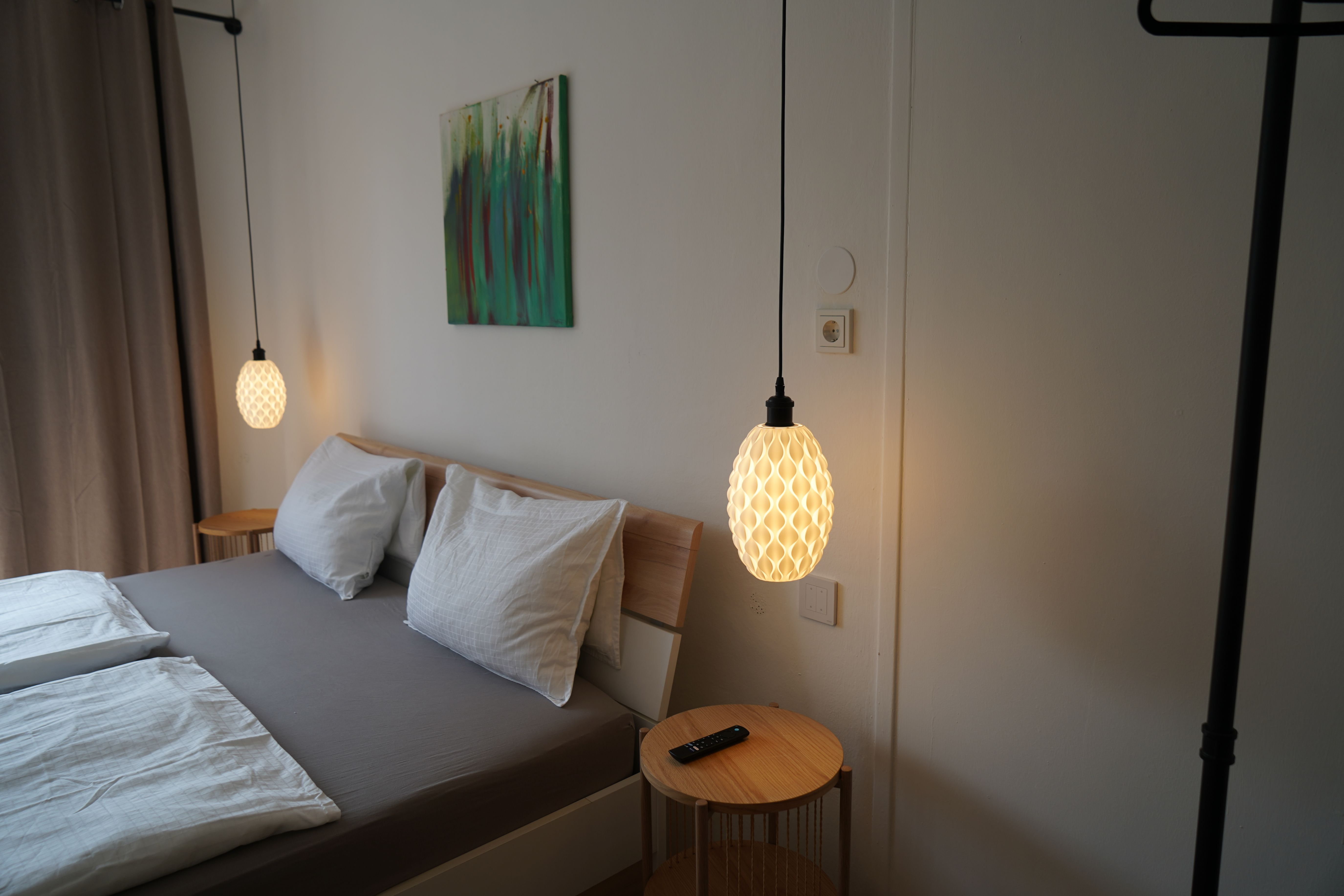 Moderní ložnice s manželskou postelí, dvěma závěsnými lampami a malým stolkem s dálkovým ovládáním.