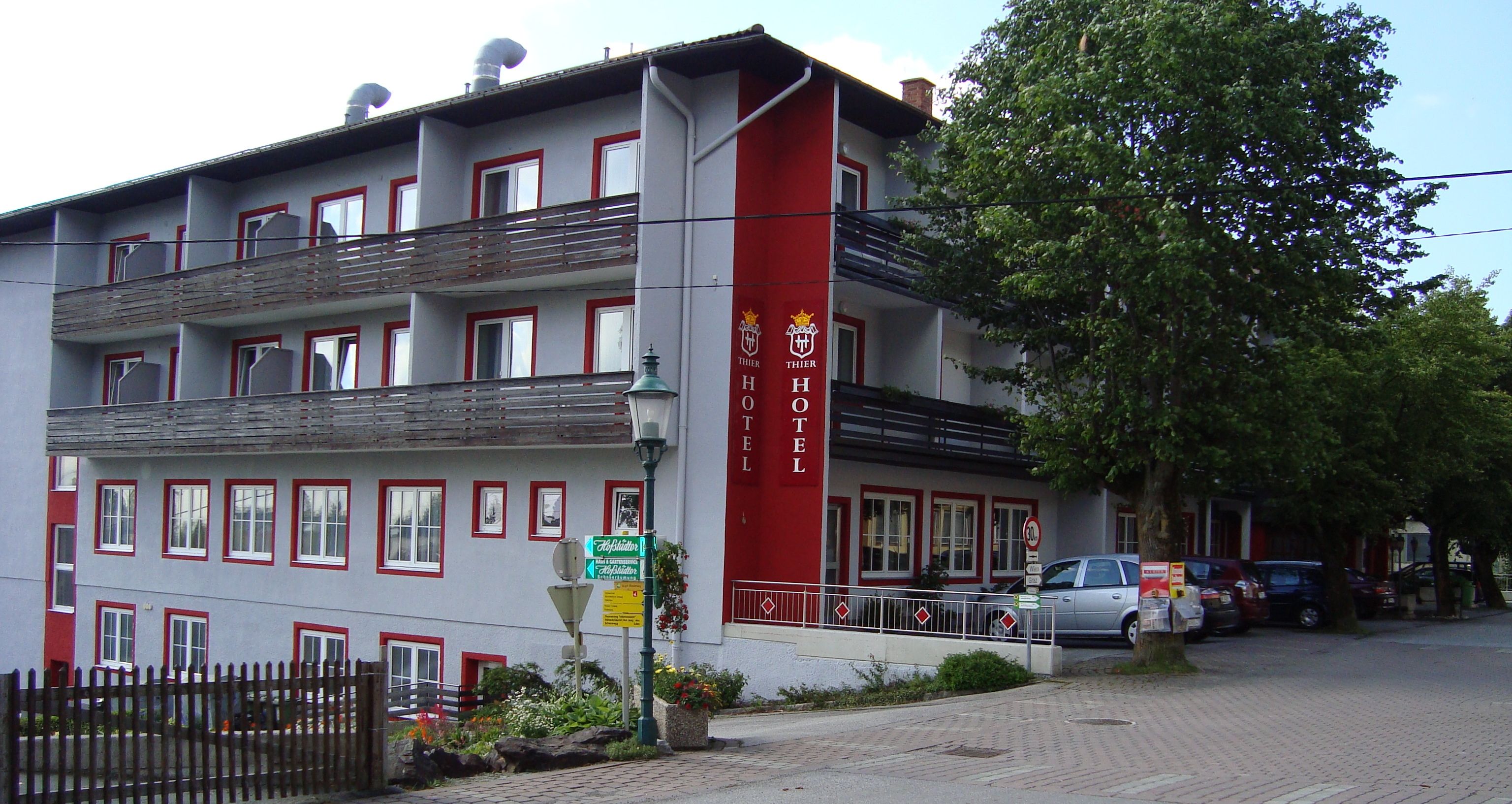 Pohled na exteriér hotelu Thier s balkony a červenými nápisy.