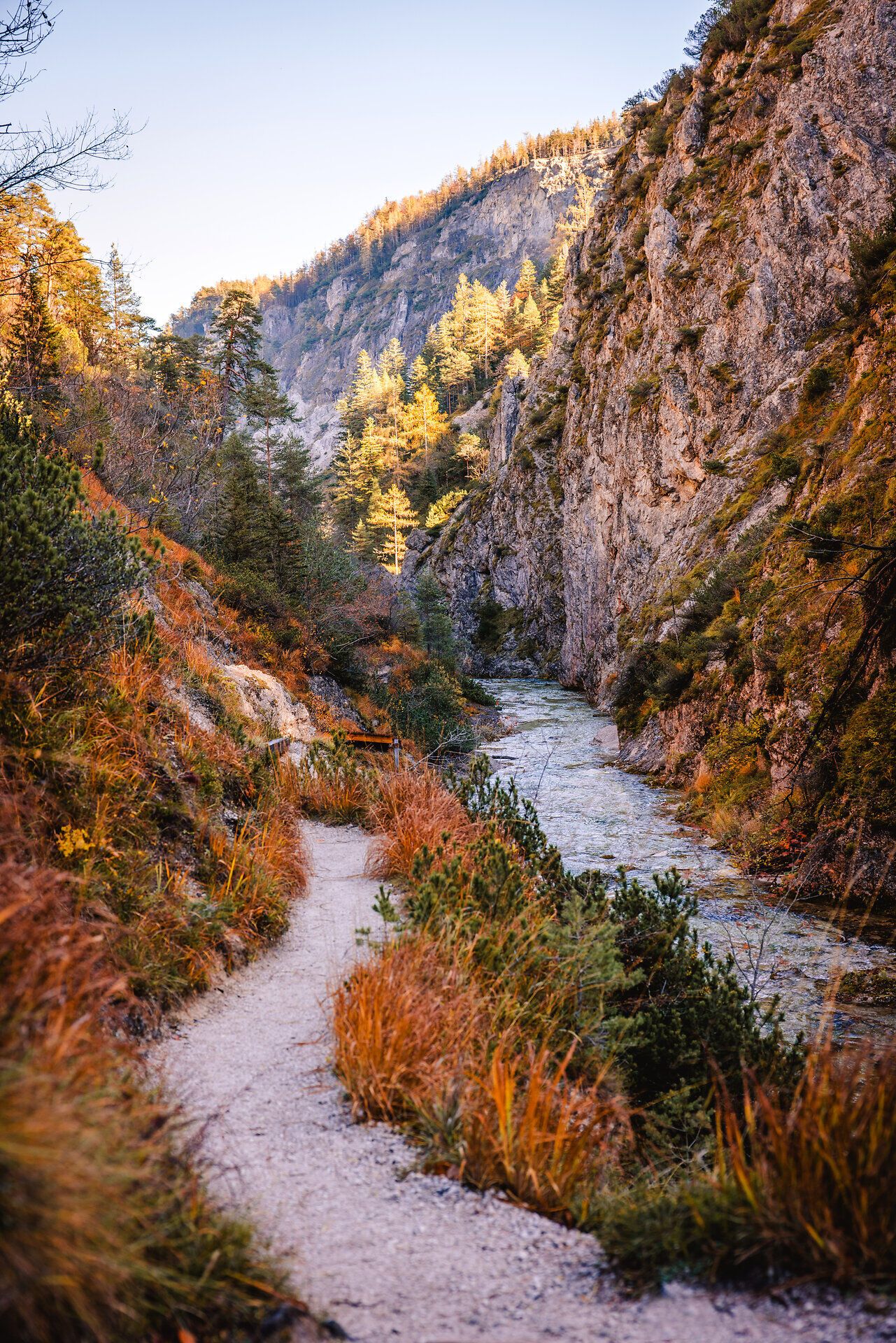 Die sanften Kurven des Pfades schlängeln sich durch die beeindruckende Schlucht, umgeben von majestätischen Felsen und leuchtenden Herbstfarben. Das glitzernde Wasser des Baches fließt ruhig und lädt zu einer erholsamen Wanderung in der unberührten Natur ein.