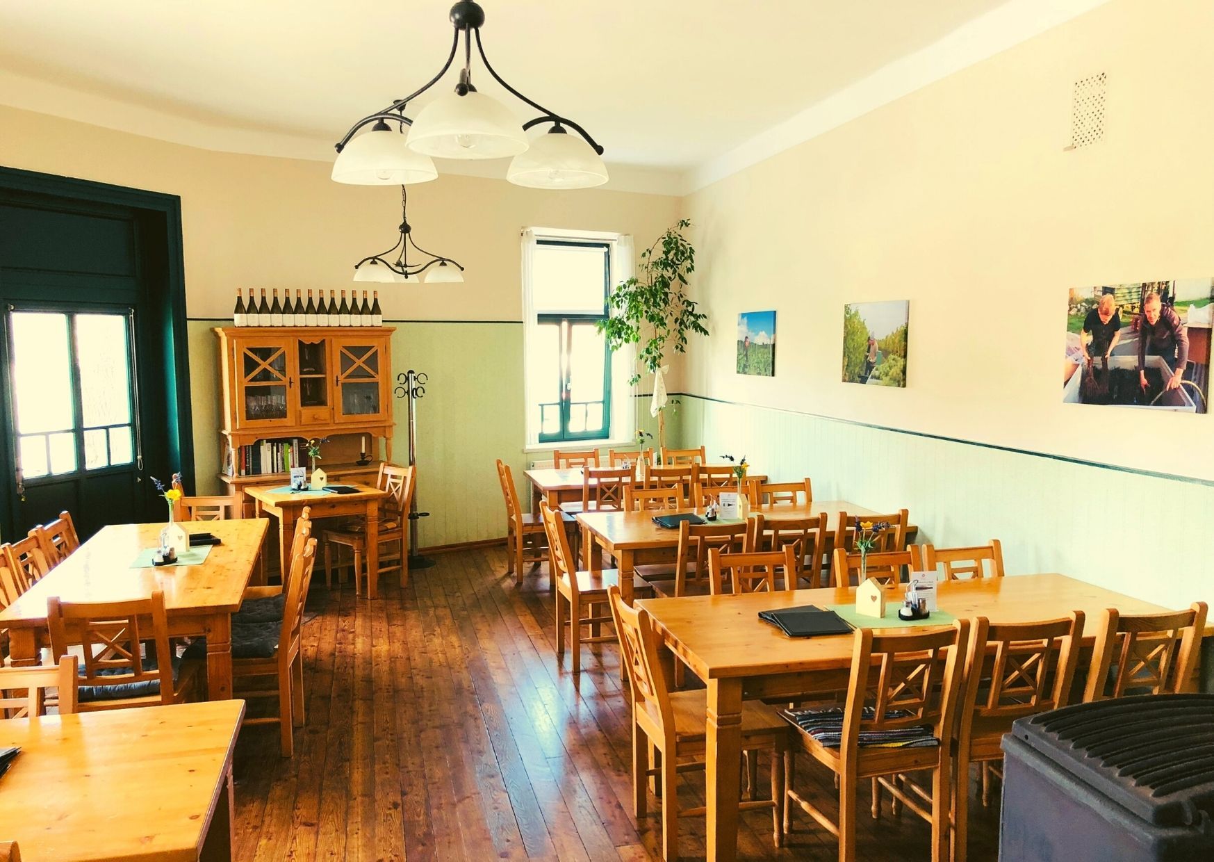 Útulná jídelna s dřevěnými stoly a židlemi, vyzdobená lahvemi vína a obrázky na stěnách.