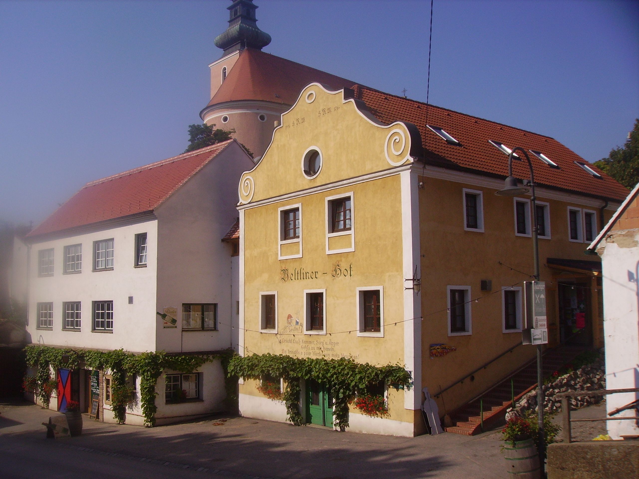 Historická budova se žlutou fasádou a červenými střešními taškami, vedle ní bílá budova. V pozadí věž s kopulí.