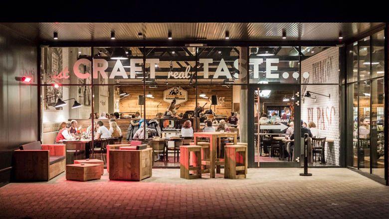 Exteriérový pohled na restauraci s proskleným průčelím a dřevěným nábytkem.