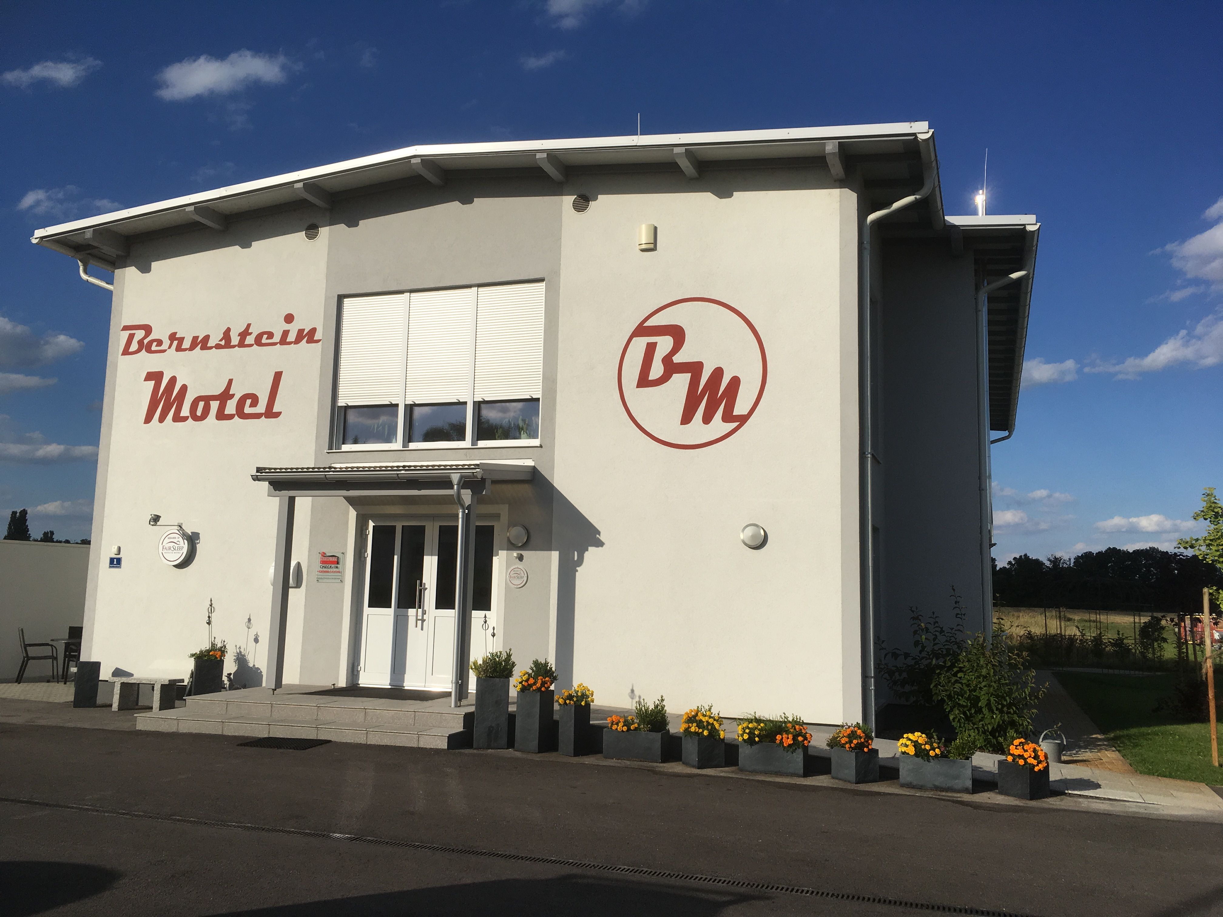 Pohled zvenčí na motel Bernstein s květinami a modrou oblohou.