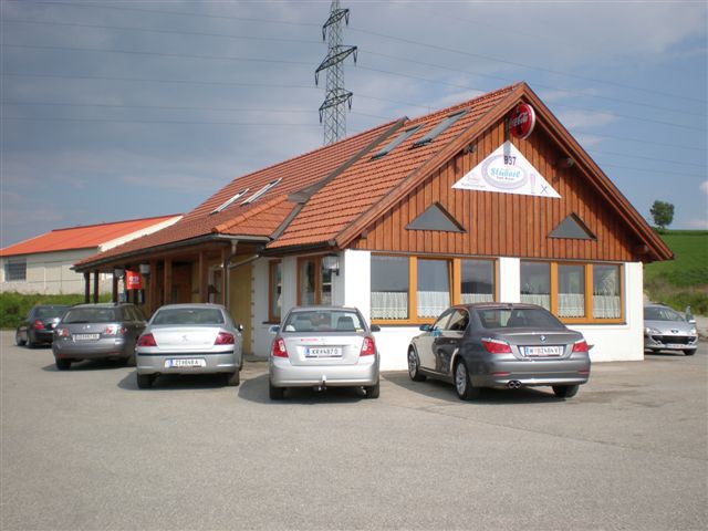 Restaurace s dřevěnou fasádou a několika zaparkovanými auty před ní.
