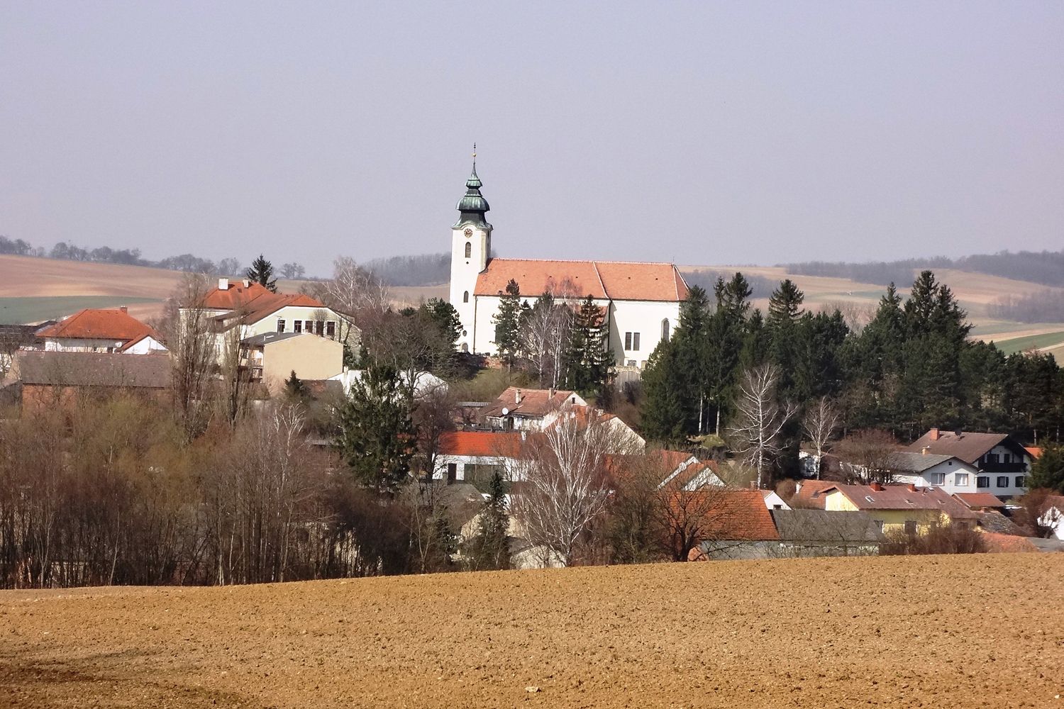 Pohled na obec Gnadendorf s kostelem a okolními domy ve venkovské krajině.