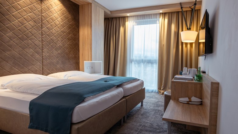 Alfred, © Niederösterreich Werbung / Maximilian Pawlikowsky Moderní hotelový pokoj s manželskou postelí, dřevěným obložením a okny se závěsy.