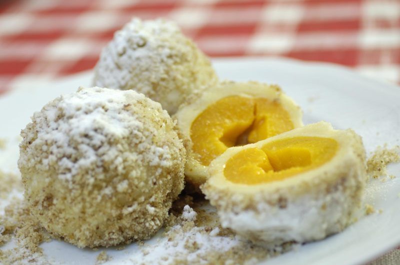 Tři meruňkové knedlíky na talíři, jeden z nich nakrájený na plátky.