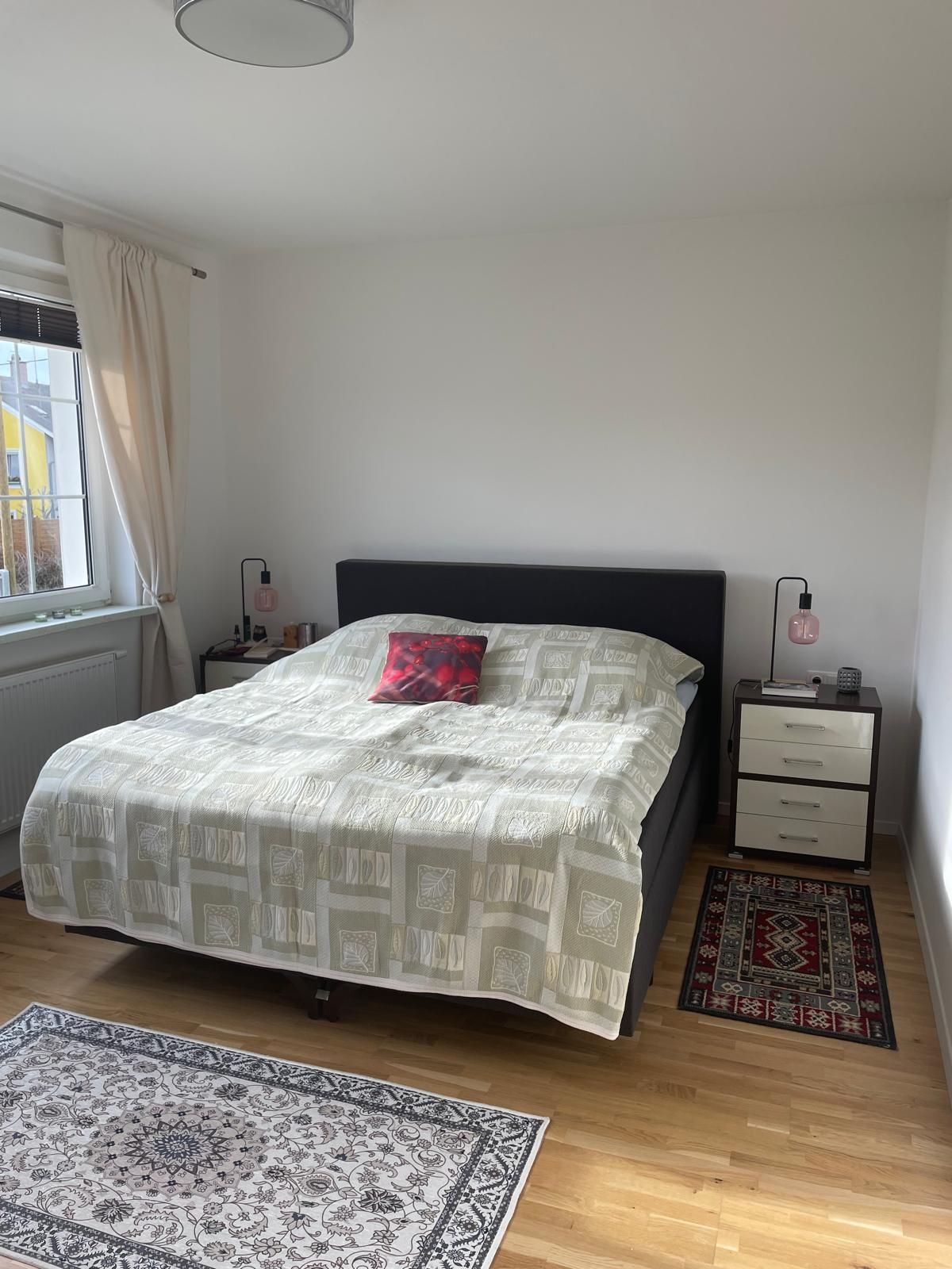 Jedna ložnice s manželskou postelí, dvěma nočními stolky a koberci na dřevěné podlaze.