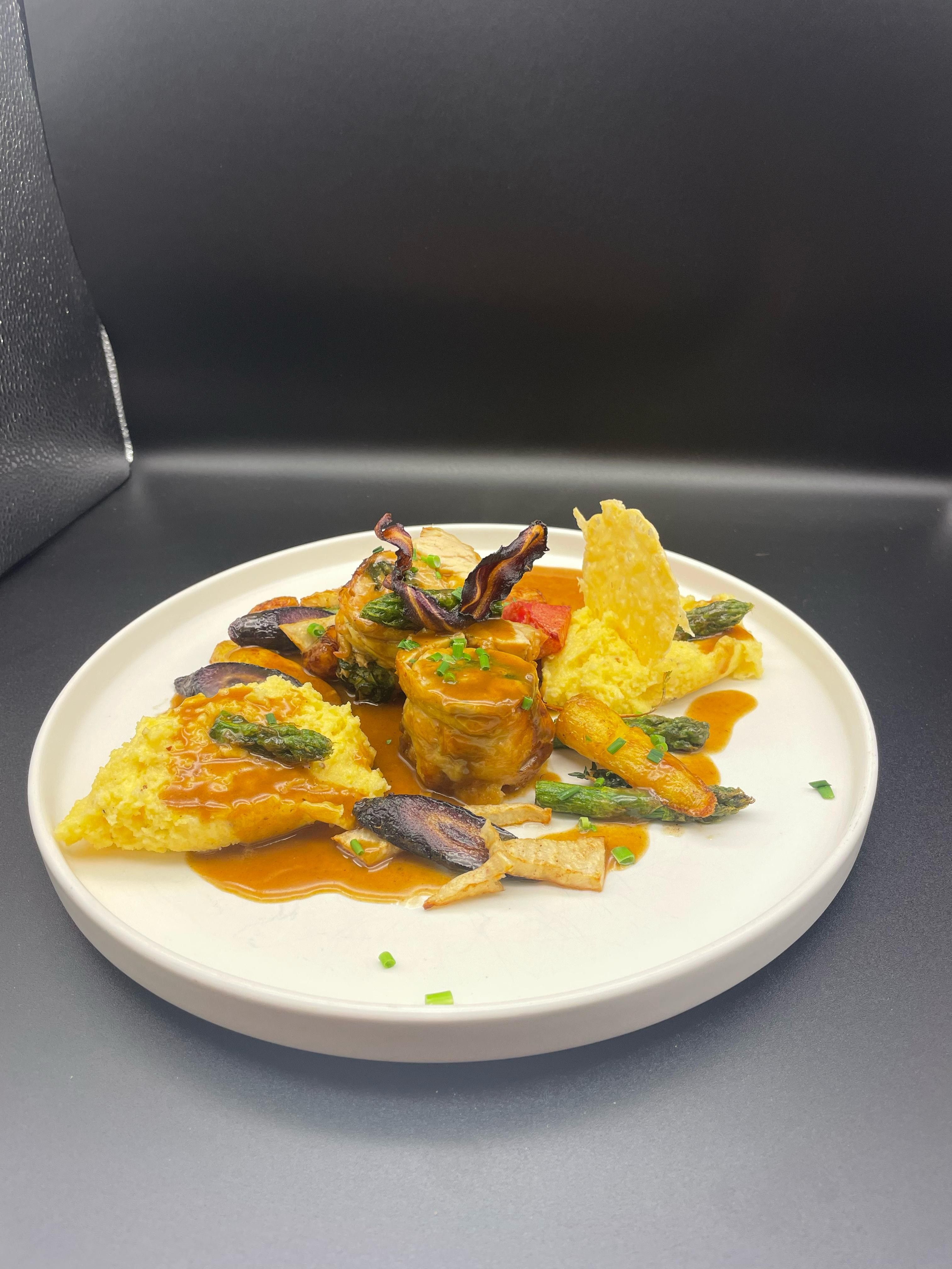 Gurmánský pokrm na bílém talíři s masem, zeleninou a omáčkou.