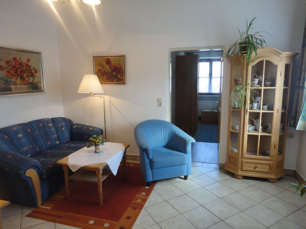 Obývací pokoj s modrou pohovkou, modrým křeslem, dřevěným stolem a vitrínou.