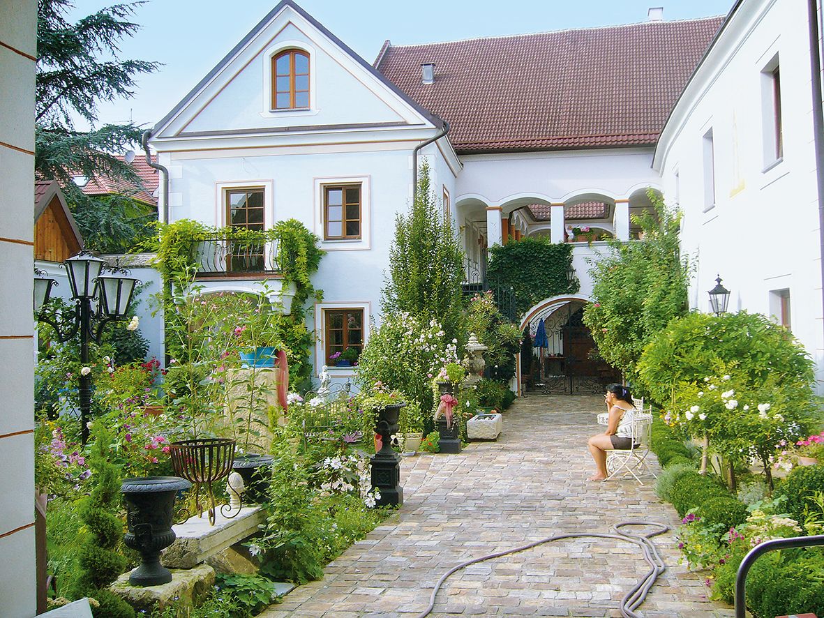 Idylické nádvoří s rostlinami a sedící osobou.