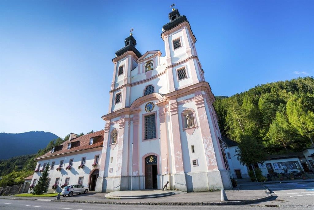 Poutní kostel Maria Schutz s modrou oblohou a zelenými stromy v pozadí.