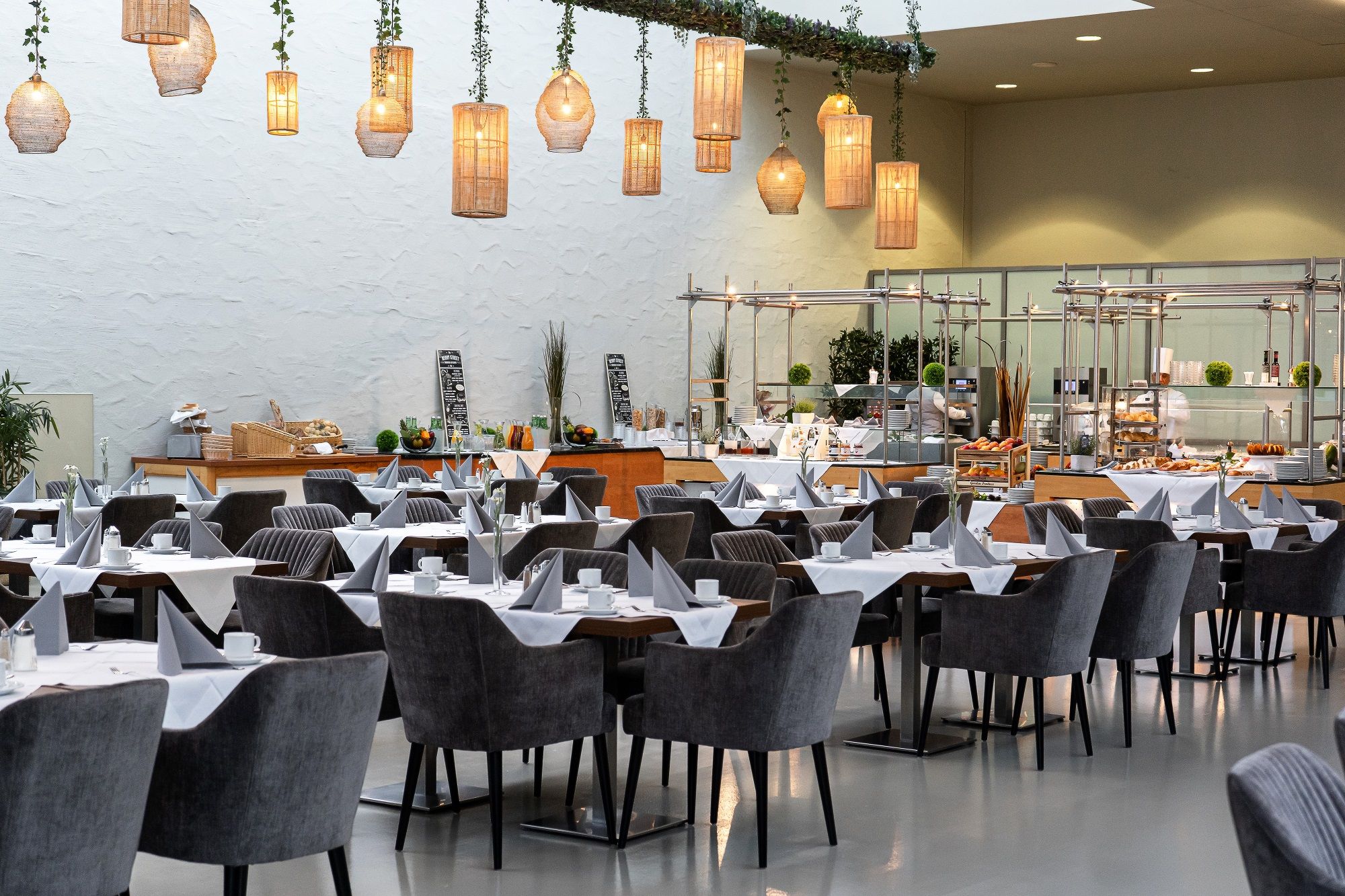 Pohled do interiéru stylové restaurace s prostřenými stoly a závěsnými lampami.
