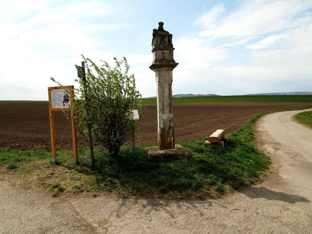 Kamenný sloup u venkovské cesty s informační tabulí a keři.