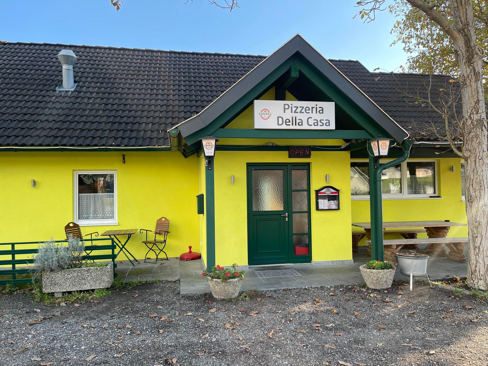 Pohled na žlutou pizzerii s názvem "Pizzeria Della Casa" zvenčí.