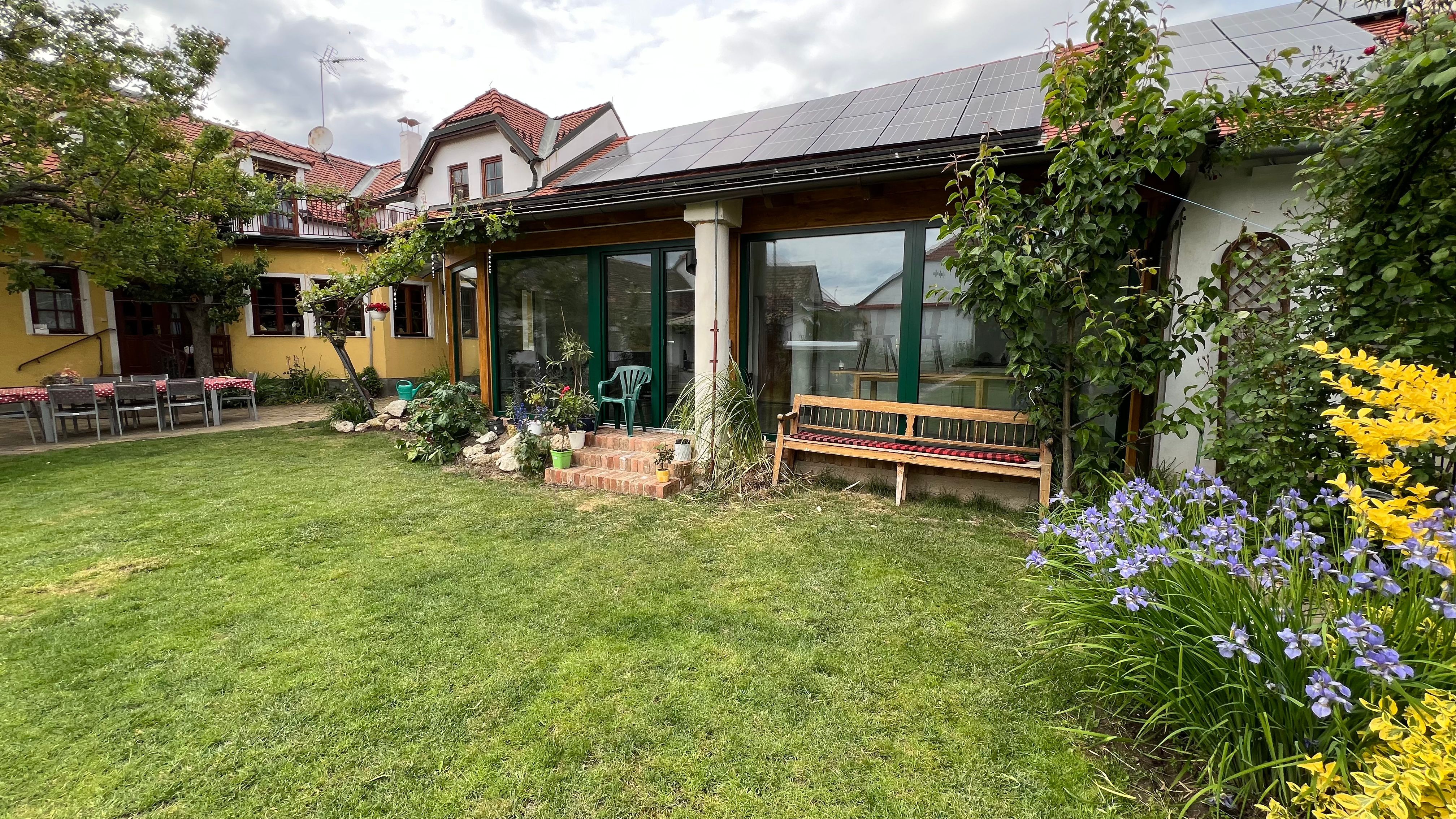 Zahrada s trávníkem, květinovými záhony a domkem se solárními panely na střeše.