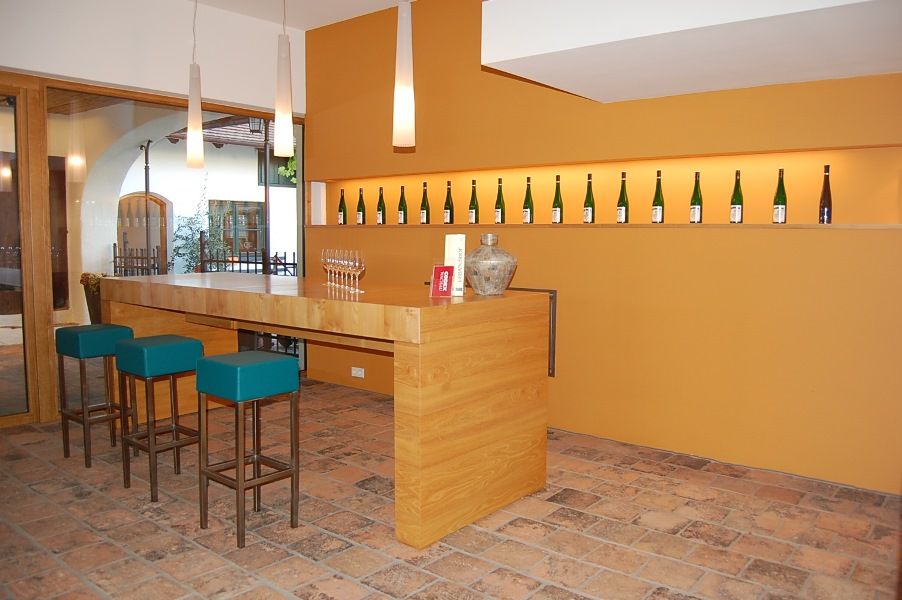 Moderní degustační místnost s dřevěným pultem, barovými stoličkami a lahvemi vína na stěně.