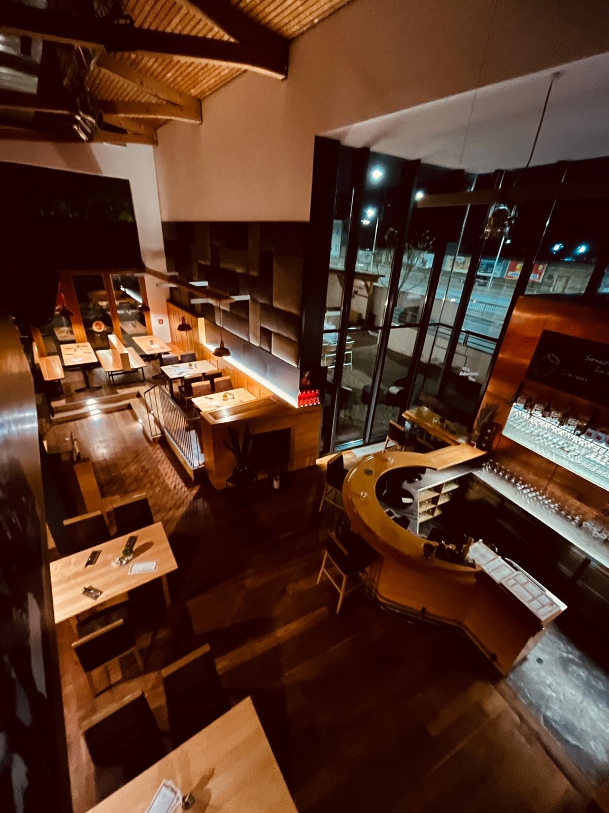 Pohled do interiéru Brauhaus Schwechat v noci s dřevěnými stoly a barem.