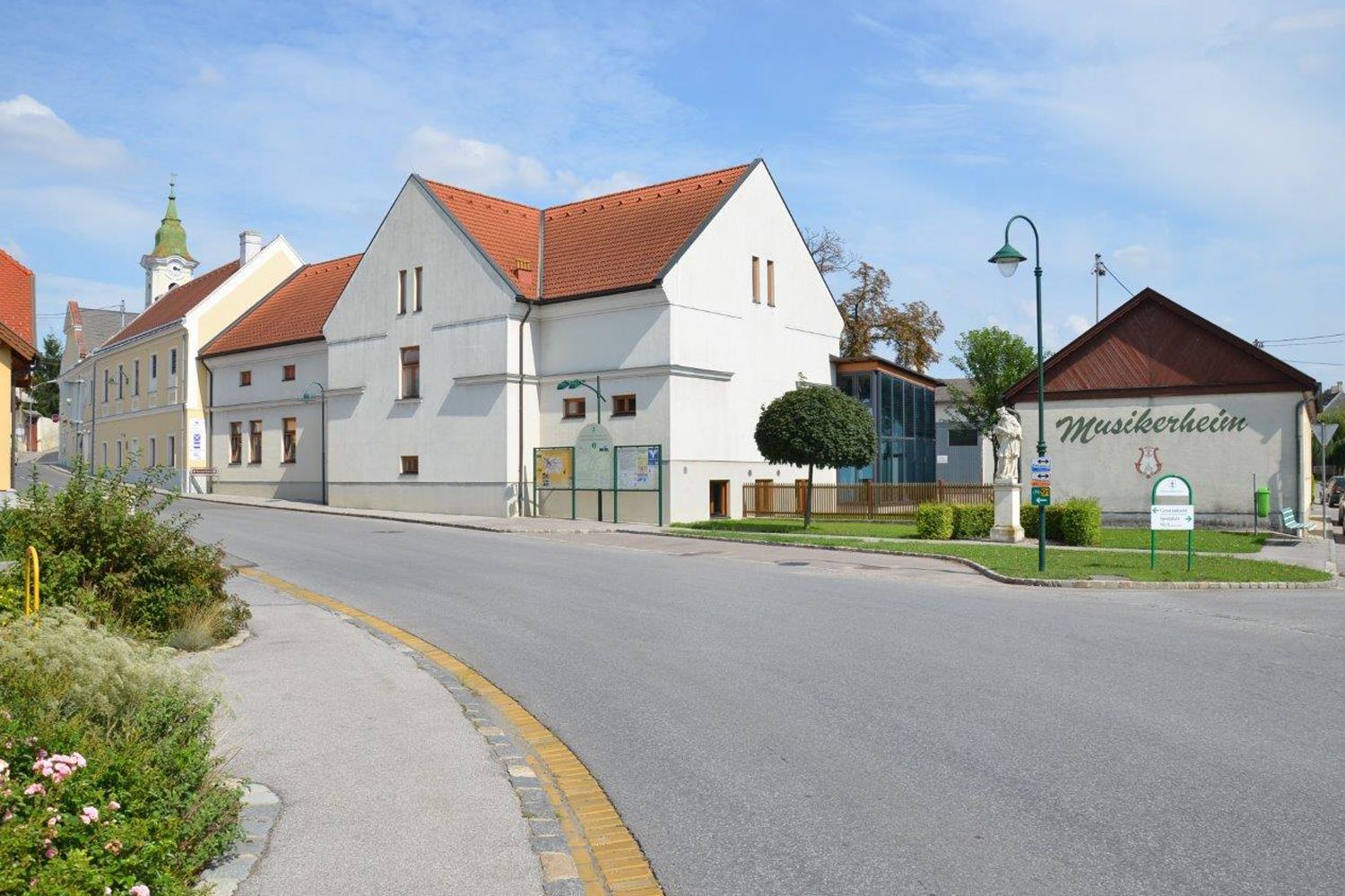 Uliční scéna v Hohenruppersdorfu s domem hudebníků a kostelem v pozadí.