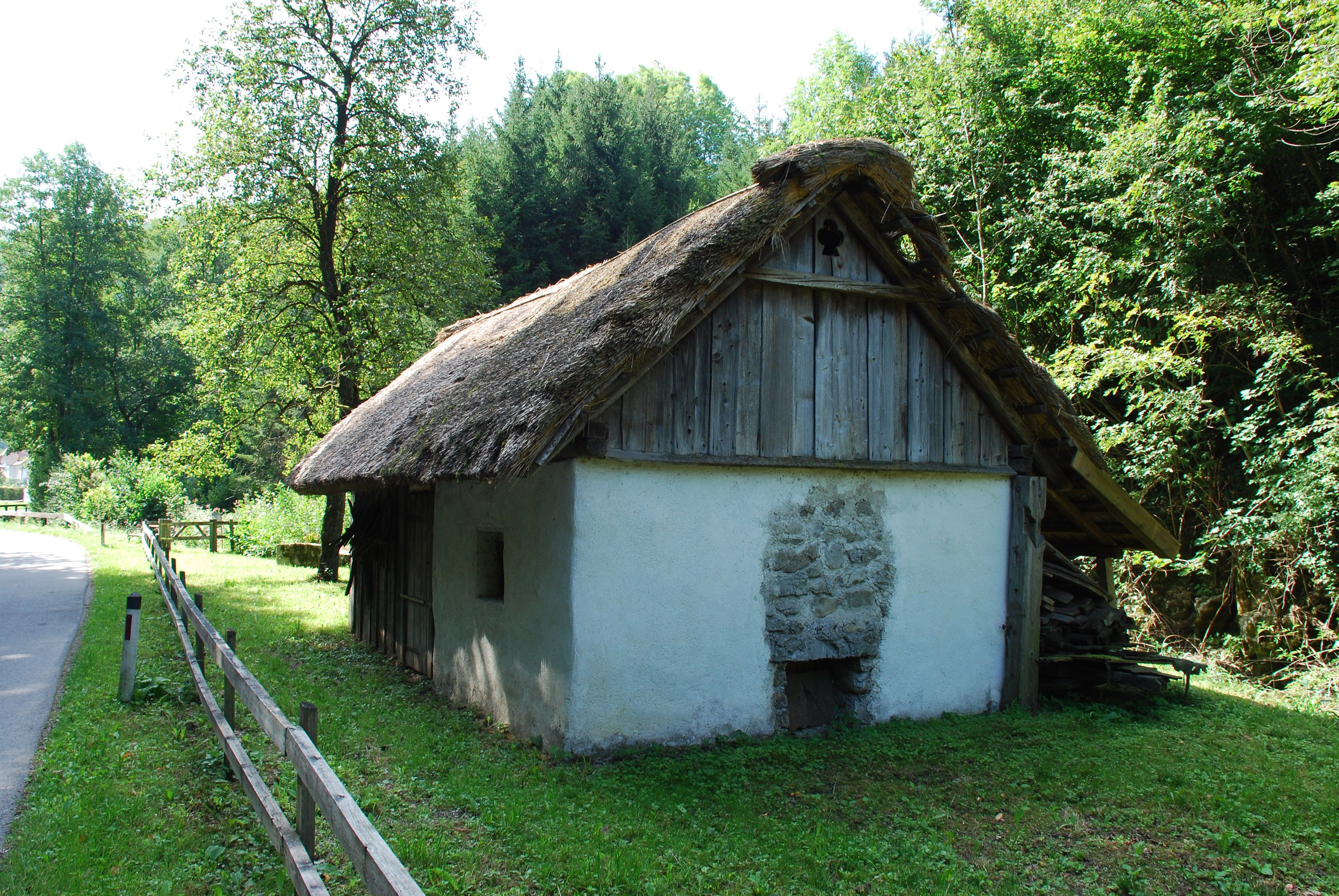 Tradiční roubená chalupa na venkově, obklopená stromy a loukami.