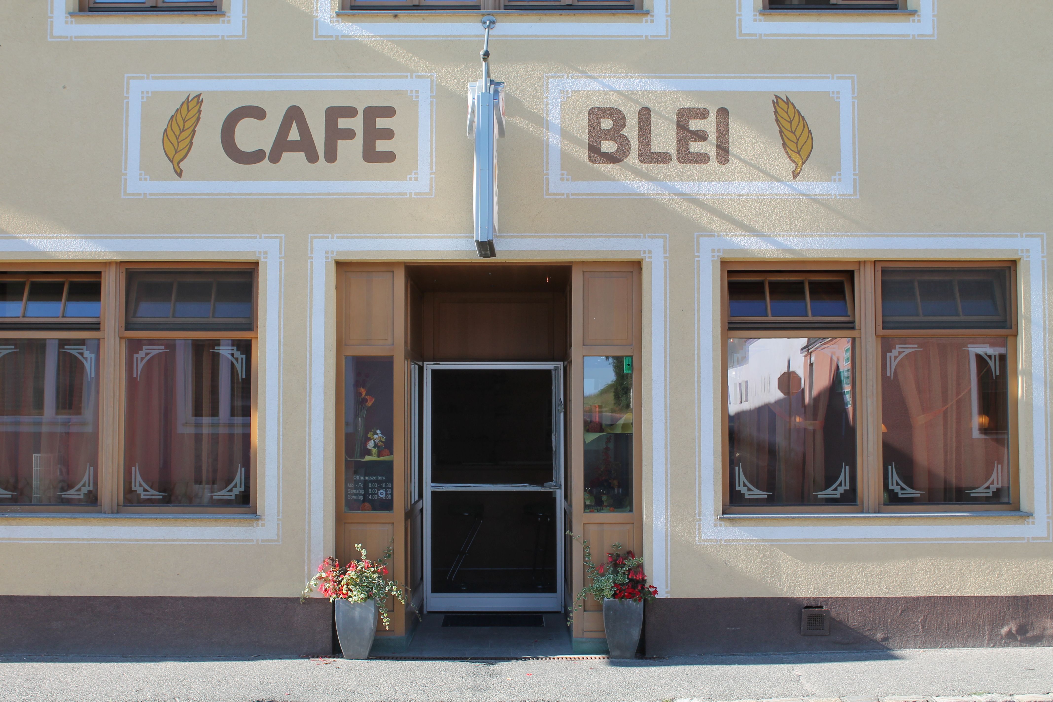 Vchod do kavárny s nápisem "Cafe Blei" a květinovou výzdobou.