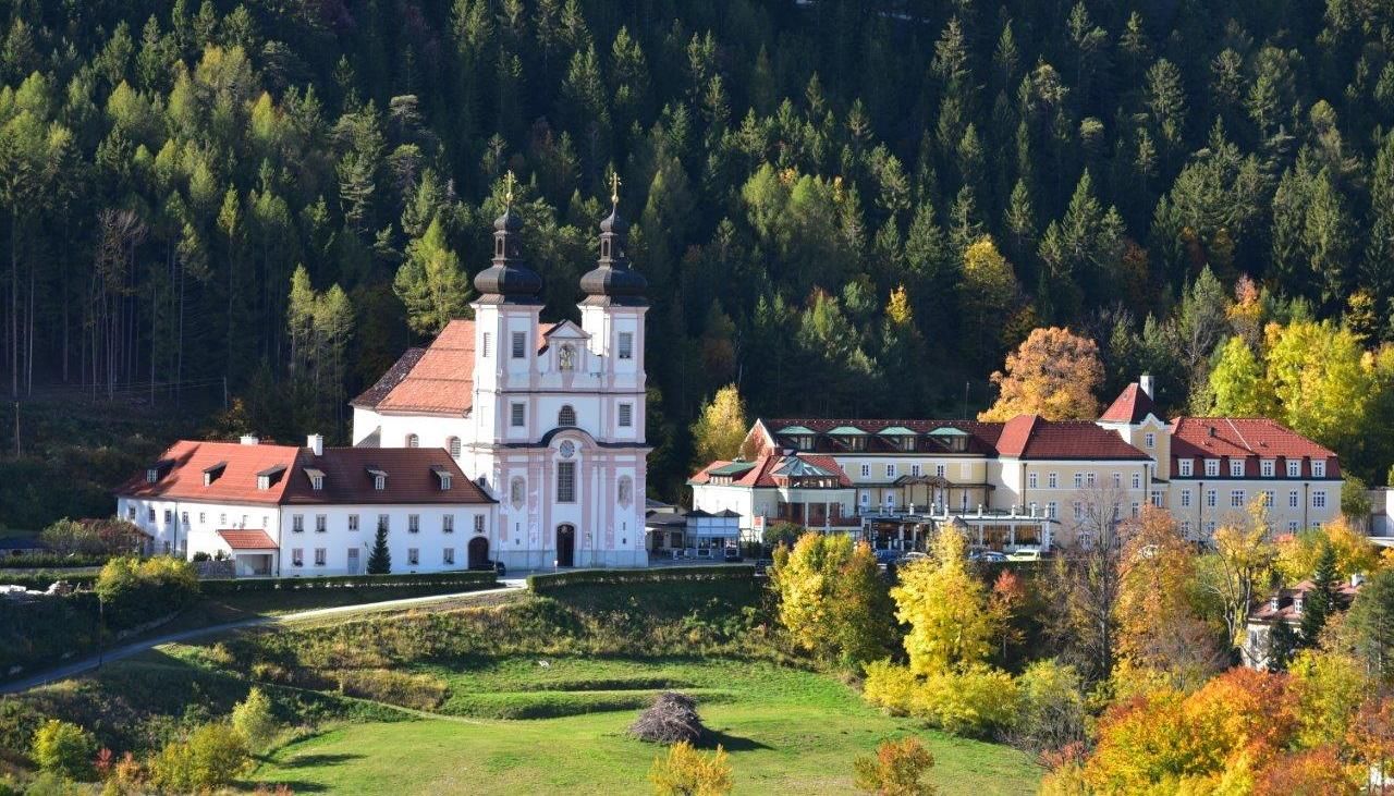 Poutní kostel Maria Schutz před zalesněným kopcem na podzim.