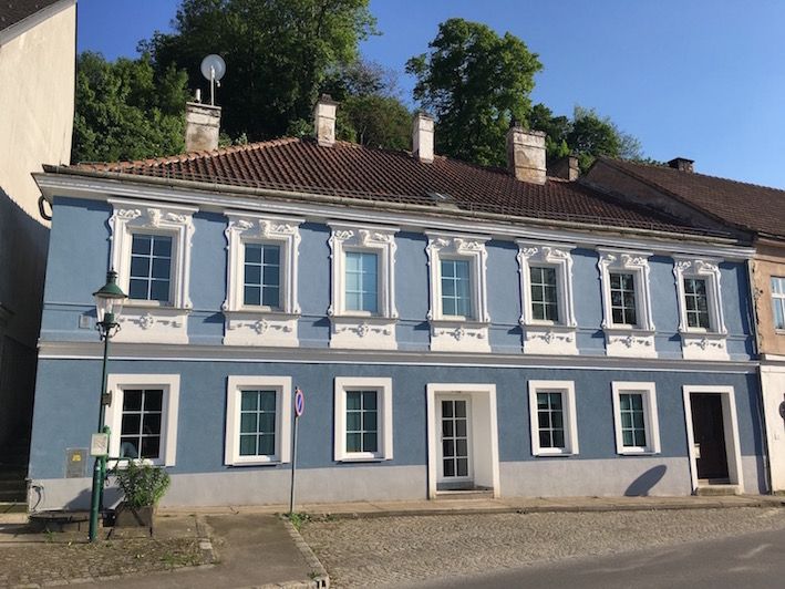 Modrá historická budova s bílými okenními rámy a taškovou střechou.