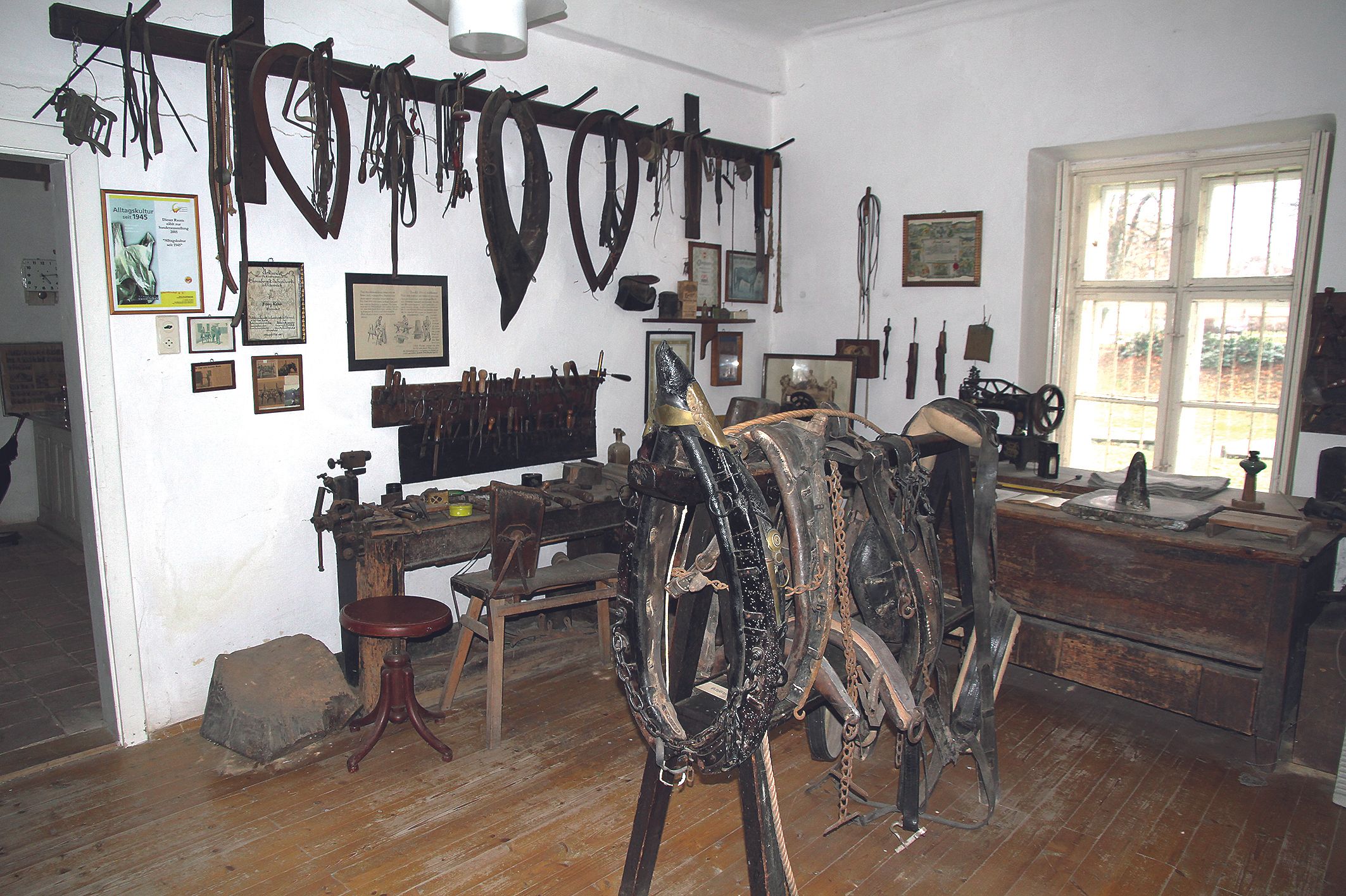 Místnost v místním historickém muzeu se starým nářadím a koňskými postroji na stěnách.
