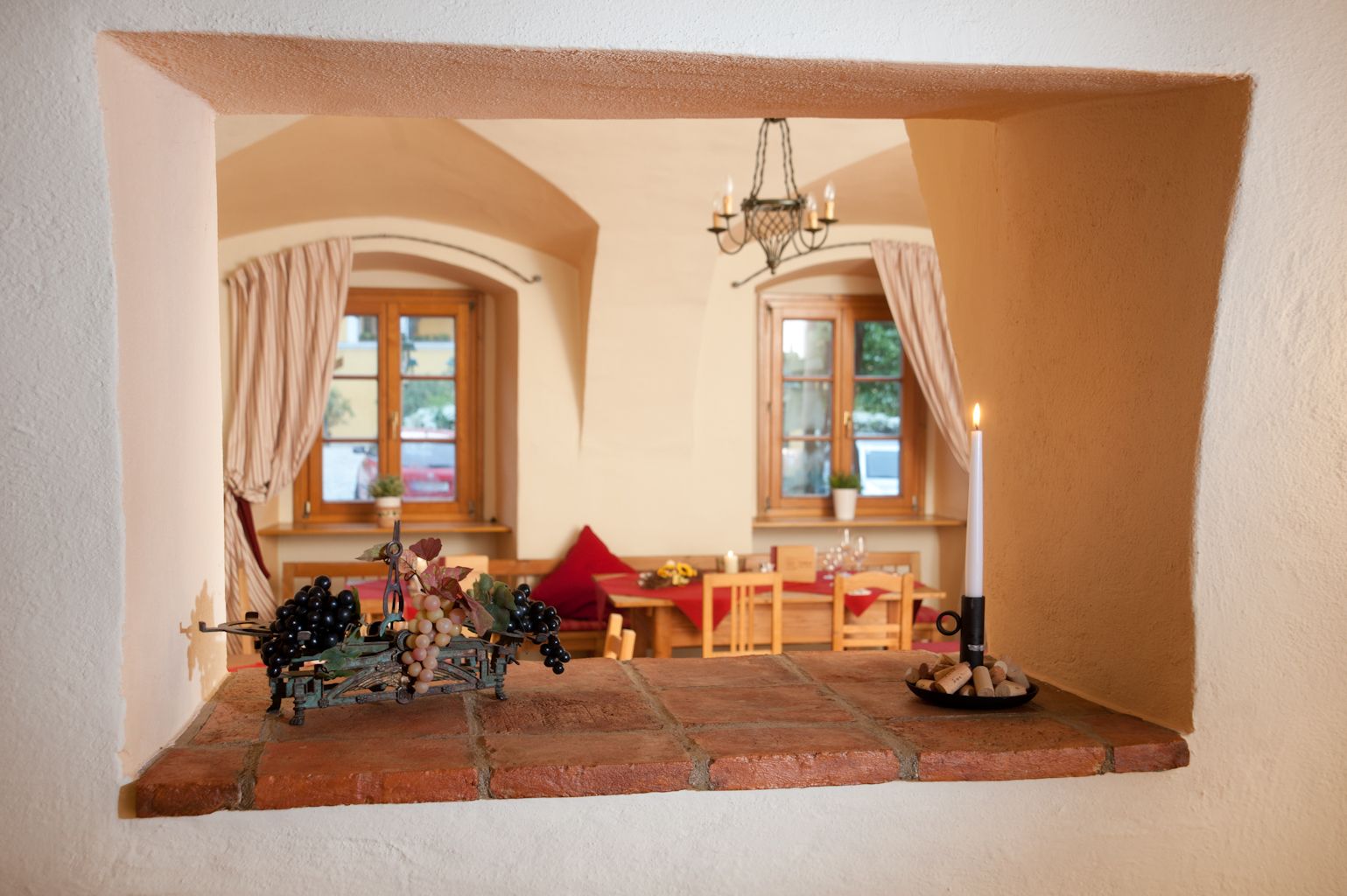 Pohled otvorem ve zdi do útulného pokoje s dřevěným nábytkem a světlem svíček.