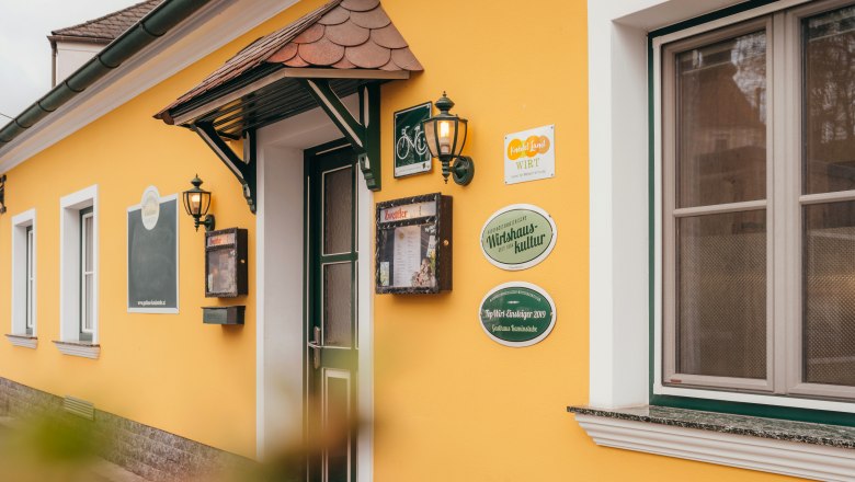 Žlutá budova s dveřmi a okny, nápisy a lucernami na zdi.