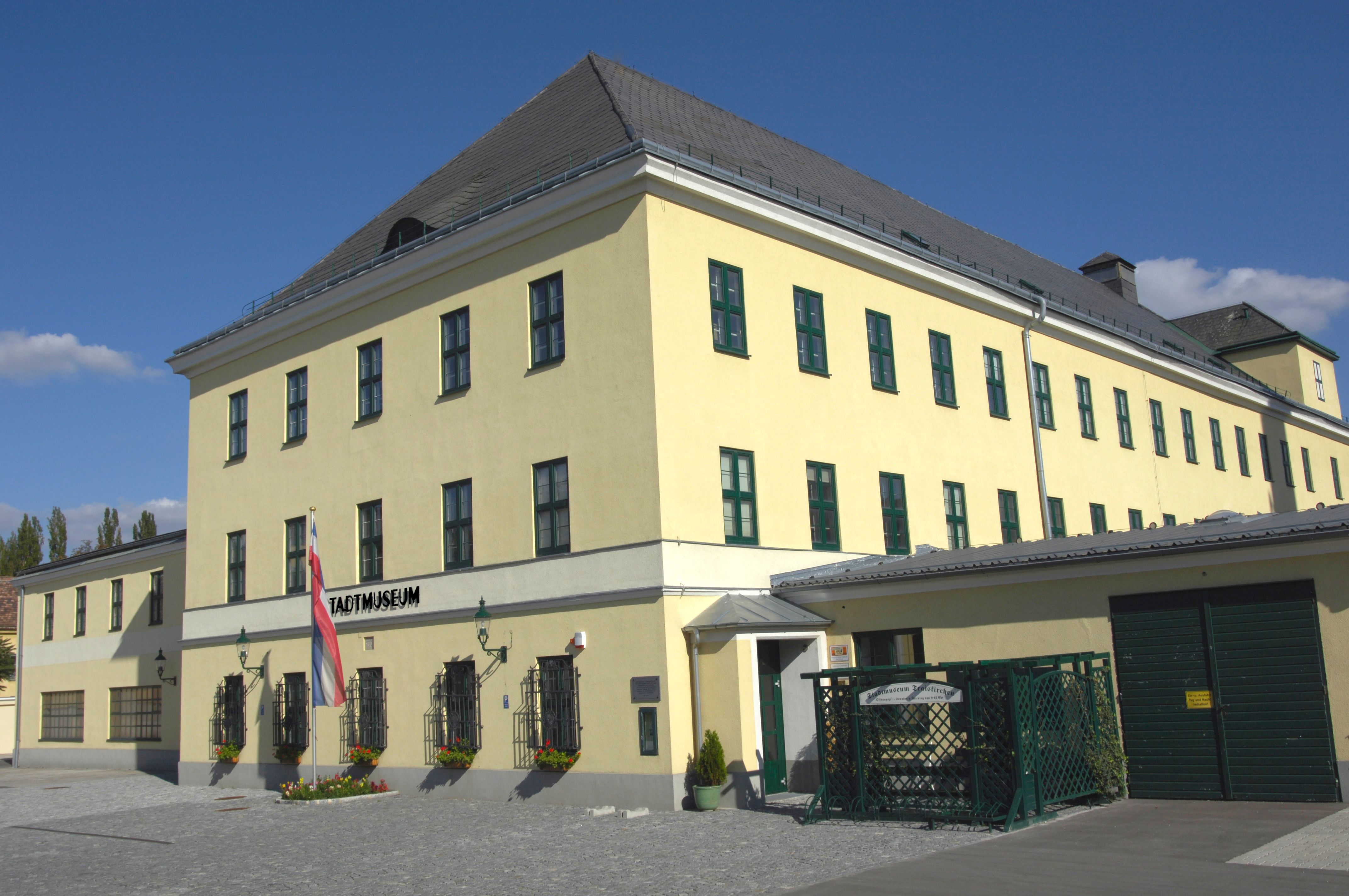 Žlutá budova s nápisem "Stadtmuseum" a rakouskou vlajkou před ní.