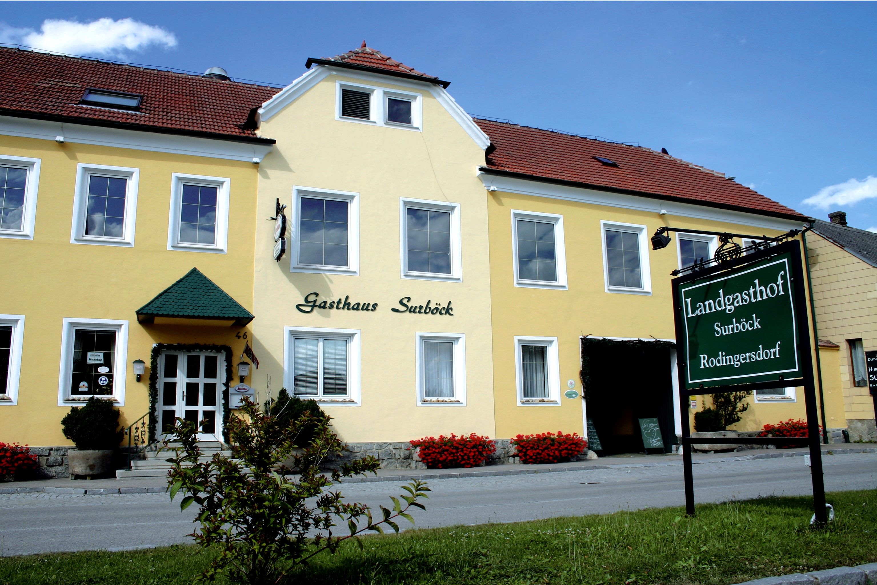 Žlutá budova s nápisem "Gasthaus Surböck" a zeleným nápisem "Landgasthof Surböck Rodingersdorf".