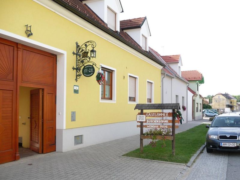 Žlutá budova s nápisem "Gästezimmer vinné šenky Weinbau Poys" a zaparkovaným autem před ní.