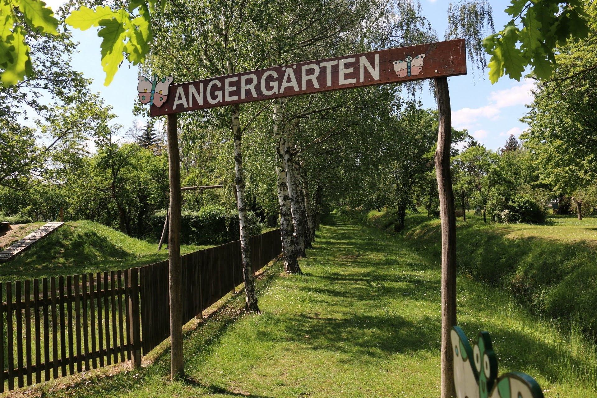 Vchod do Angergärten s dřevěnou cedulí a stromy v pozadí.