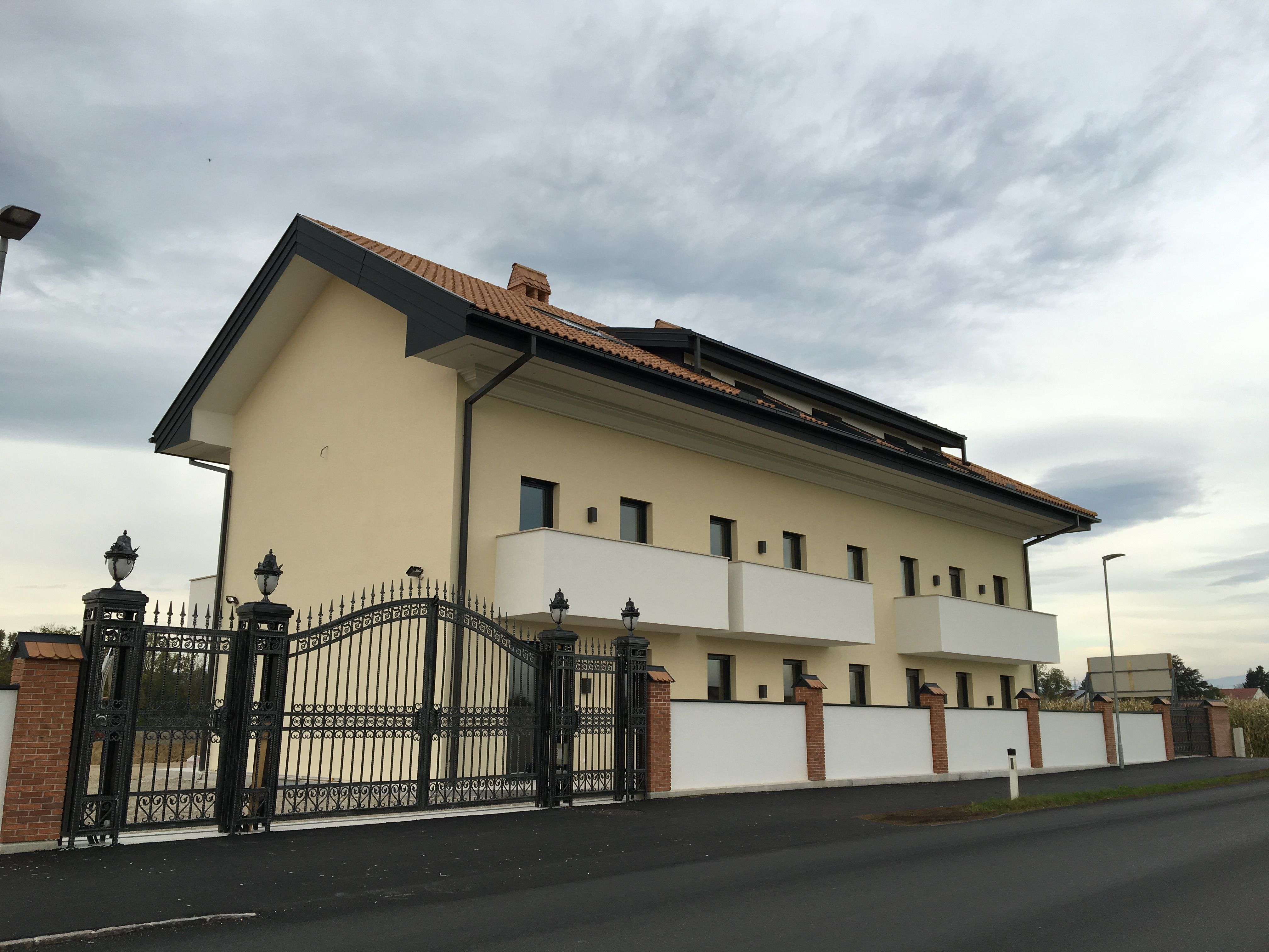 Pohled zvenčí na moderní budovu s taškovou střechou a kovanou bránou.