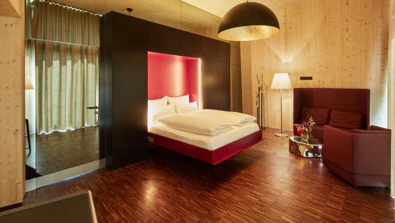 Pohled do interiéru moderní ložnice s plovoucí postelí, dřevěným obložením a stylovým osvětlením.