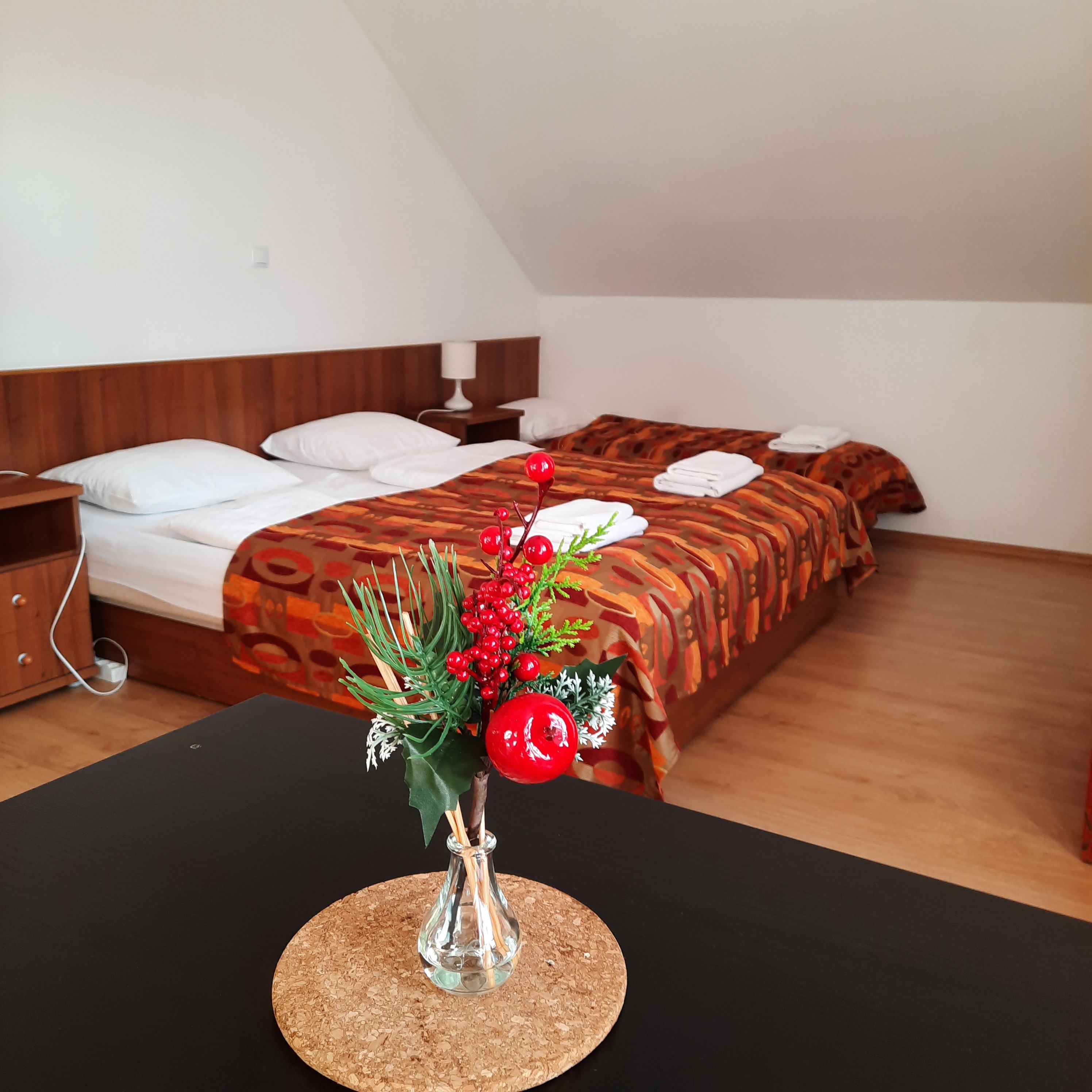 Útulná ložnice se dvěma postelemi, zdobená červenými bobulemi ve váze v popředí.