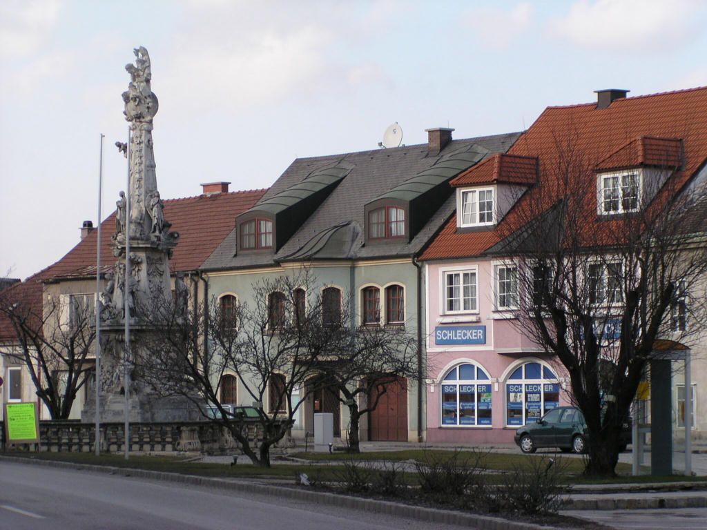 Uliční scéna v Ebenfurthu s historickými budovami a sochou.
