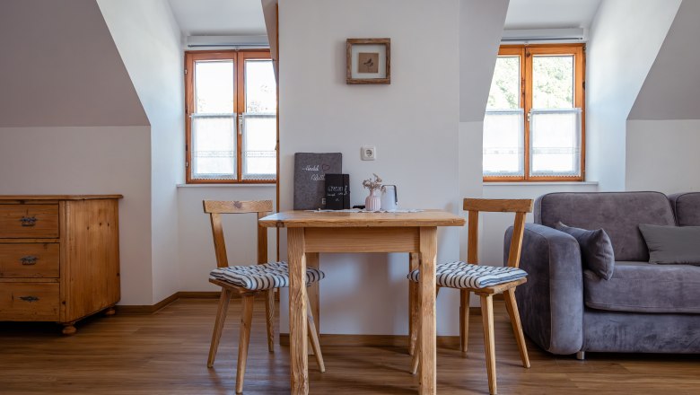 Útulný obývací prostor s dřevěným stolem, dvěma židlemi a pohovkou.