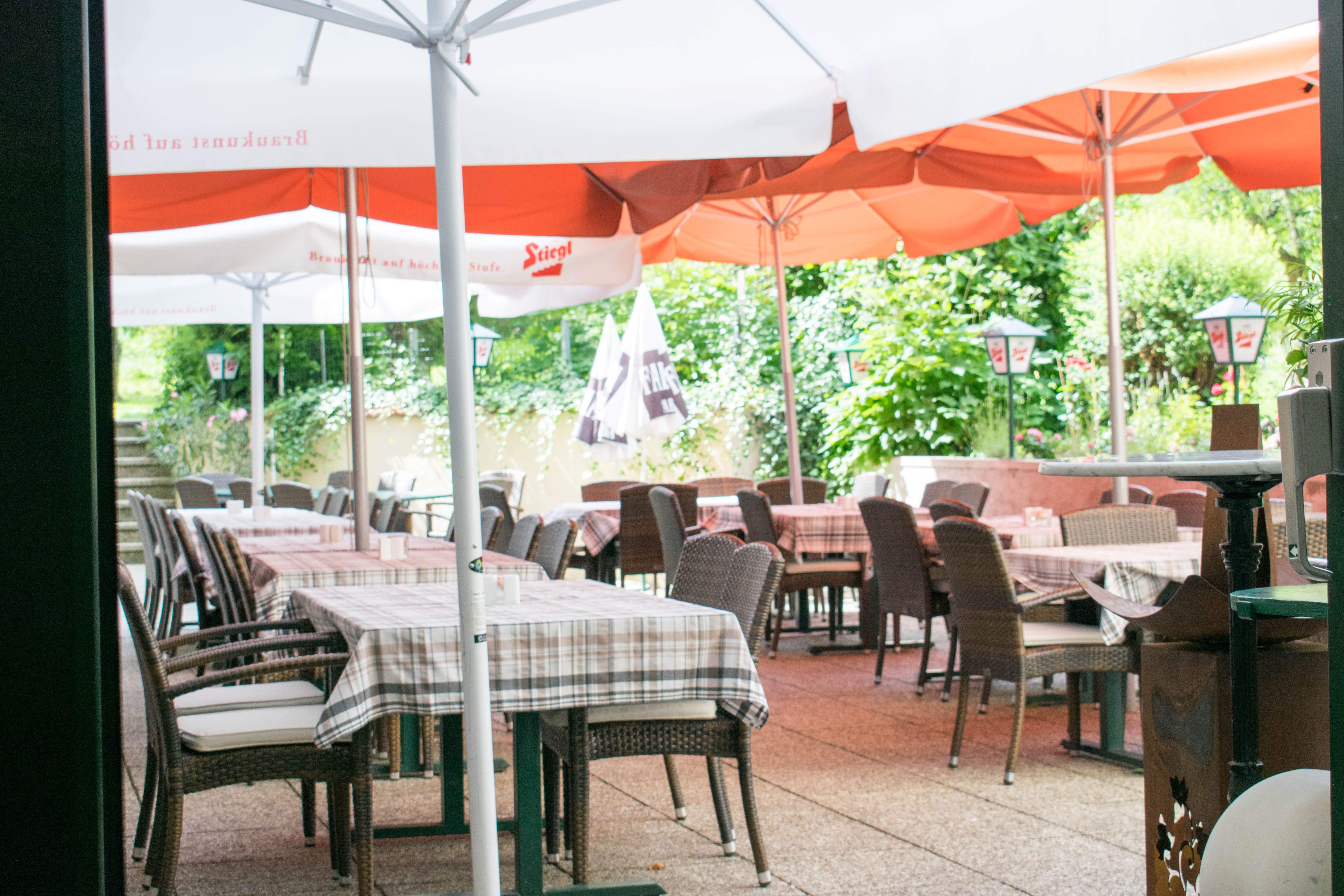 Venkovní prostor kavárny se stoly, židlemi a slunečníky.
