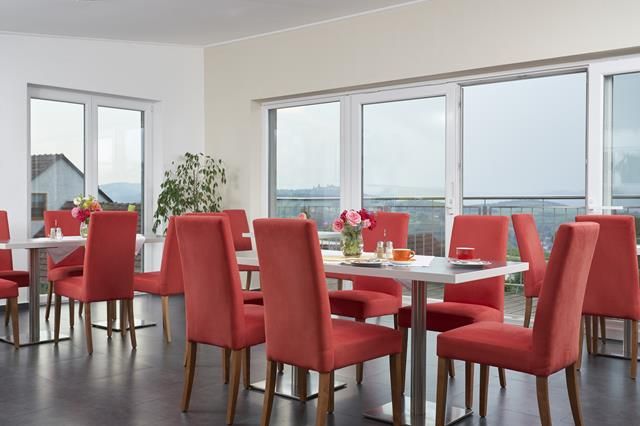 Snídaňová místnost s červenými židlemi, dřevěným nábytkem a kávovarem.