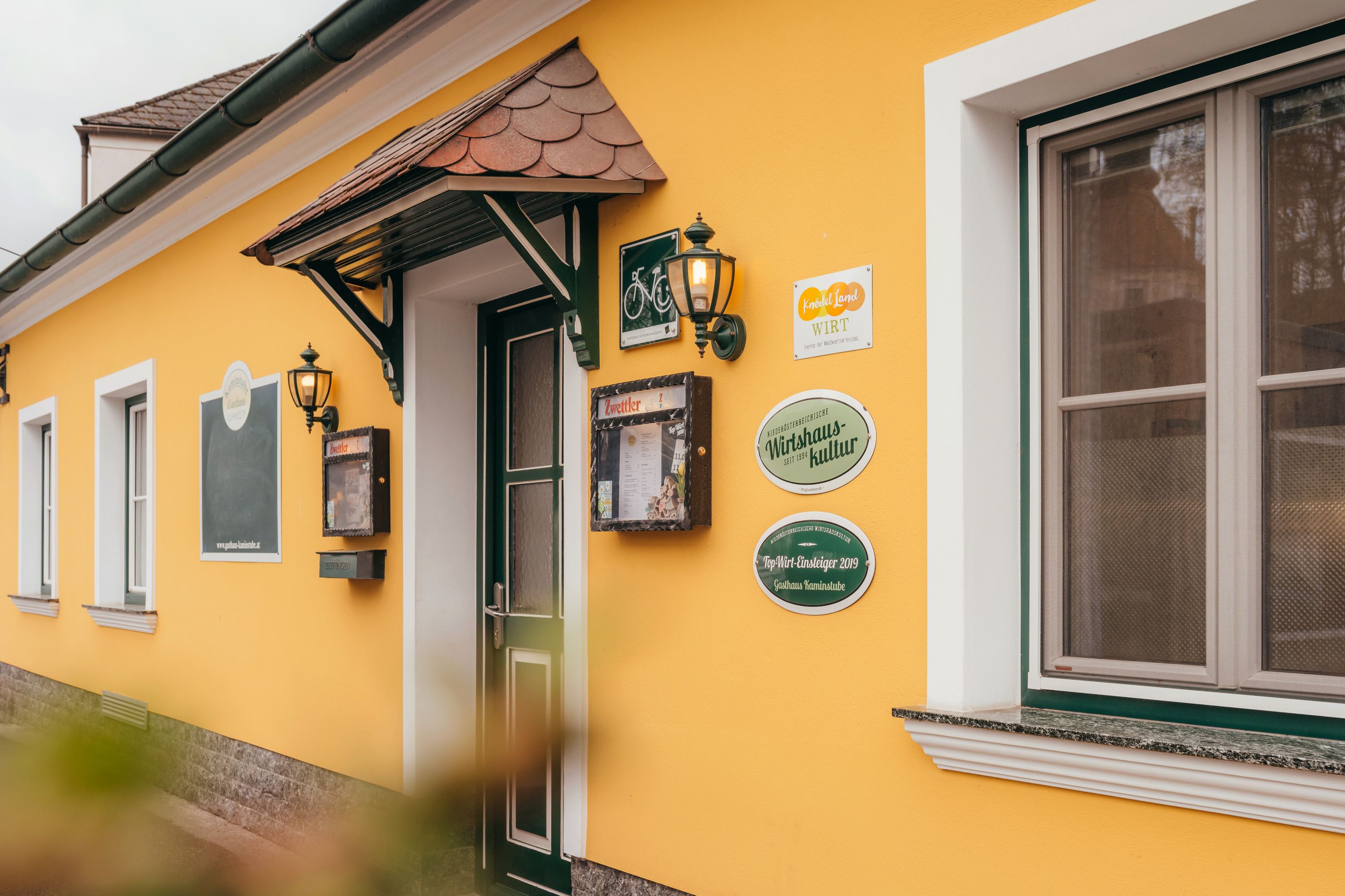 Žlutá budova s dveřmi a okny, nápisy a lucernami na zdi.