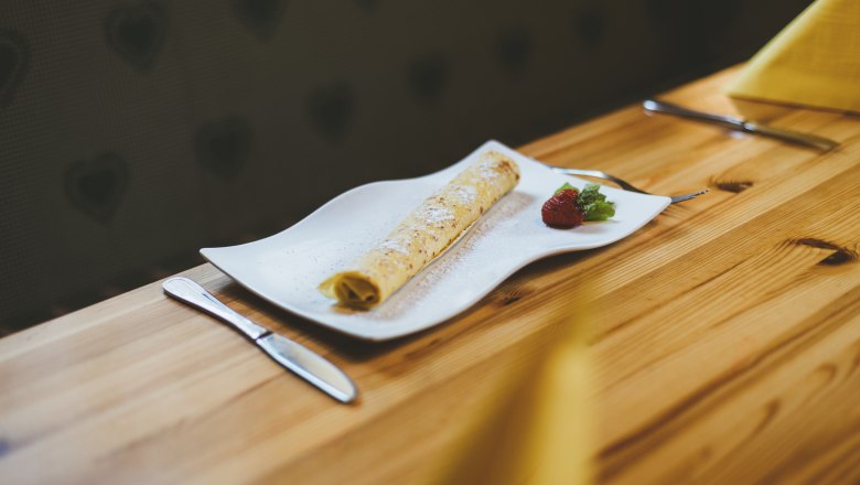 Palačinka na bílém talíři s jahodami a mátou, podávaná na dřevěném stole.