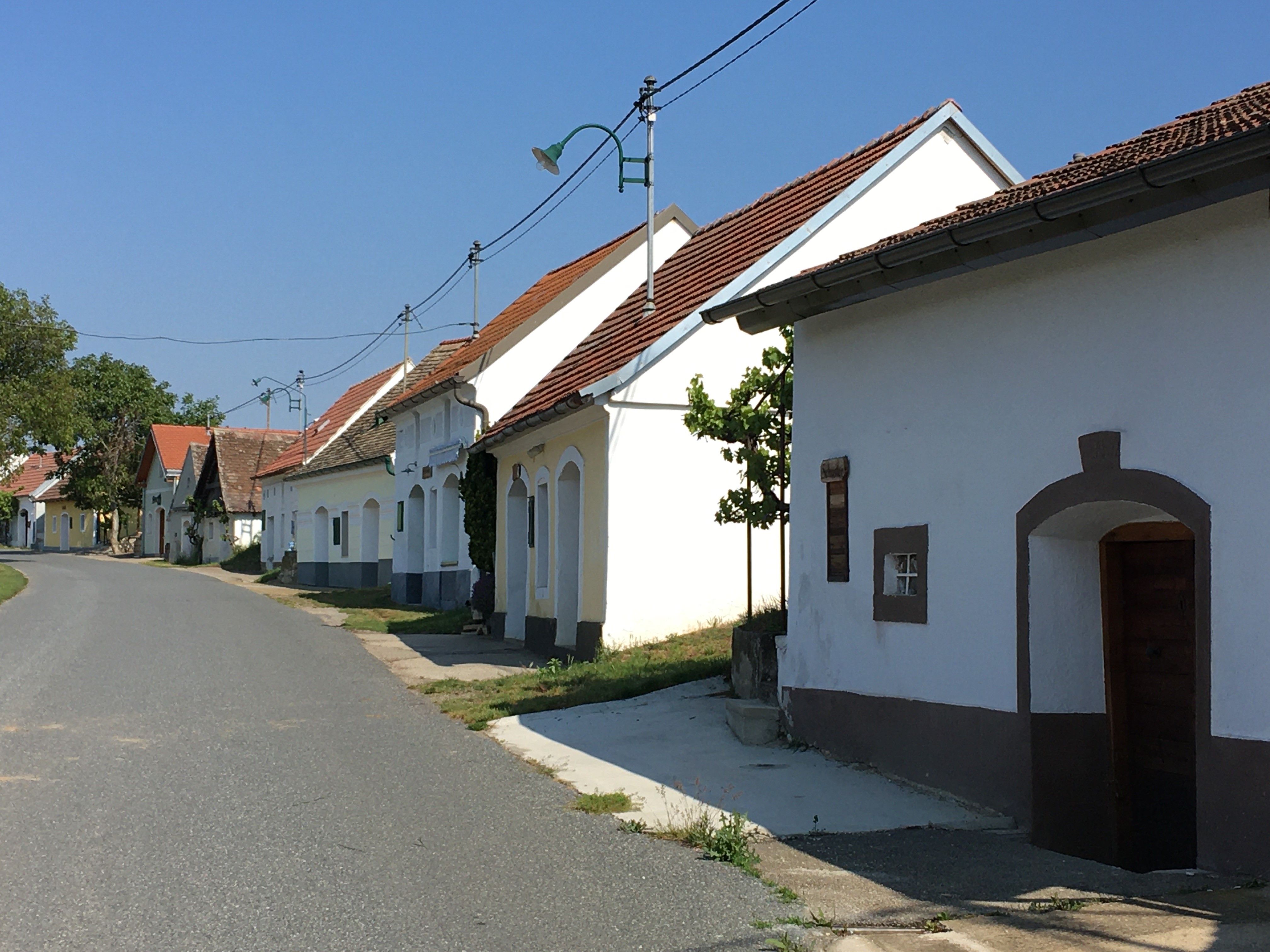 Klidná ulice s tradičními obílenými domy a červenými střechami ve venkovském prostředí.