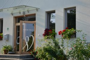 Vchod do budovy s nápisem "wein + bett", obklopený květinami.